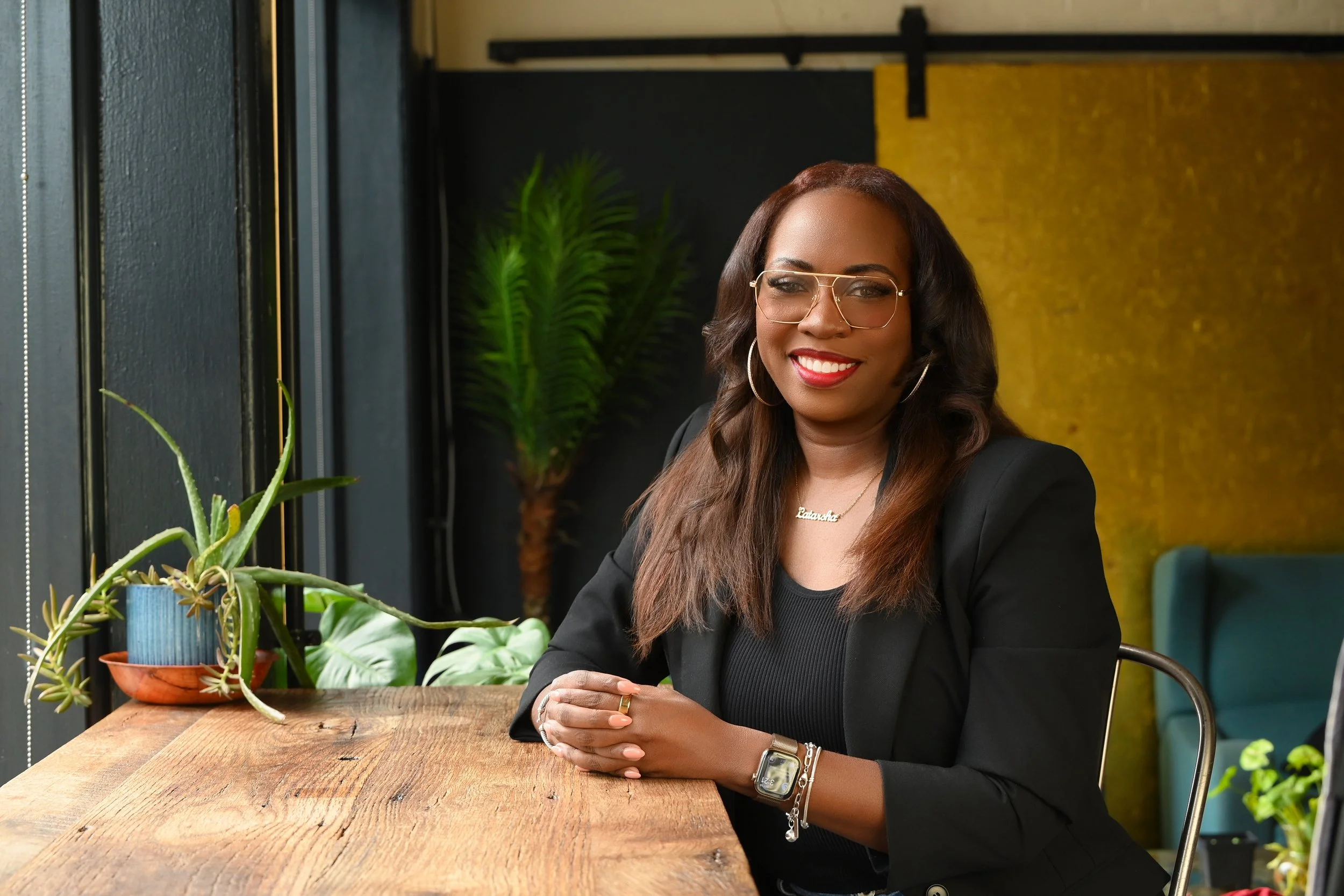 Latarsha, founder of Seen & Developed Co., seated at a wooden table in a creative workspace.