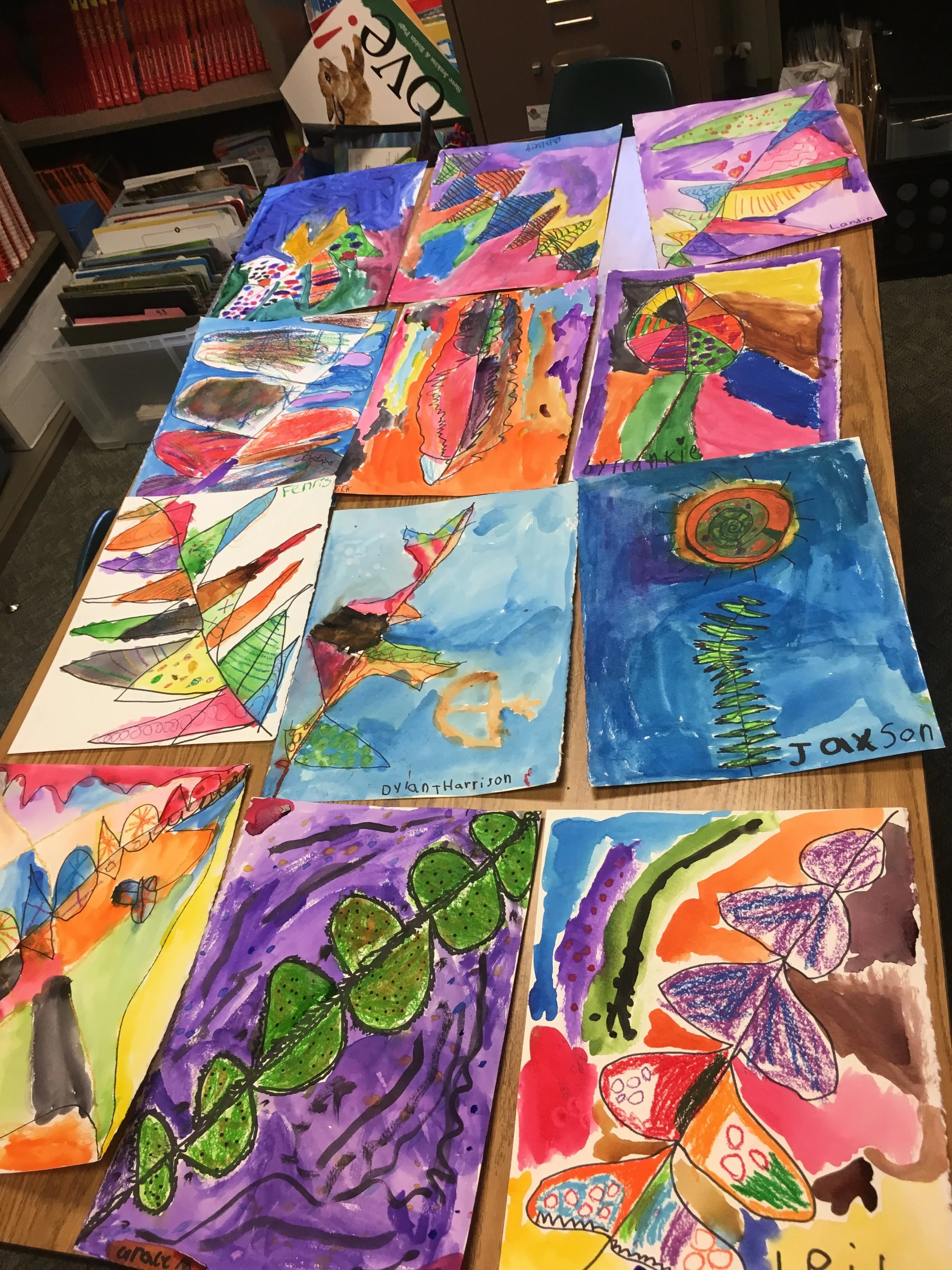 A table covered in colorful kids' artwork: butterflies, leaves, and abstract designs.