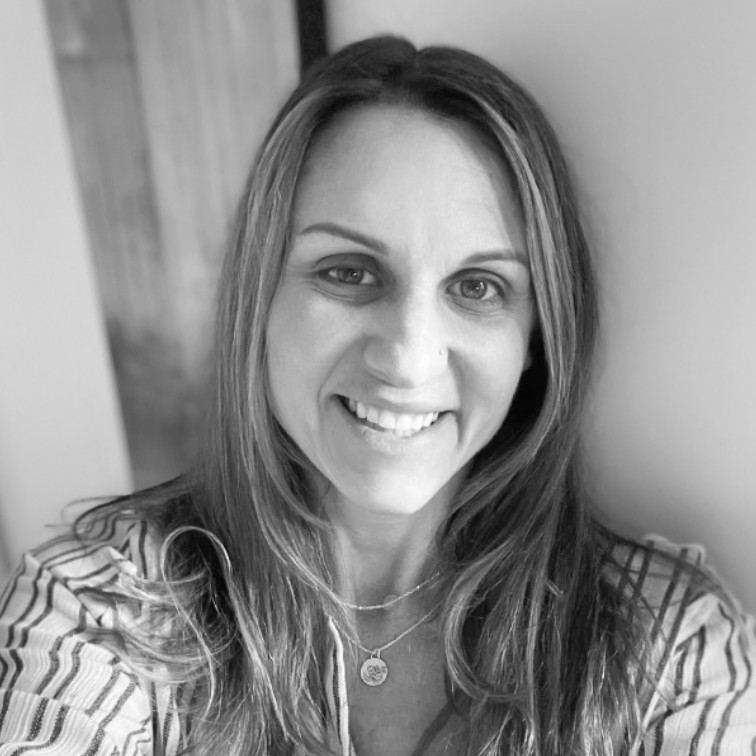 Black and white photo of a woman with long hair, smiling and wearing a striped shirt and layered necklaces.