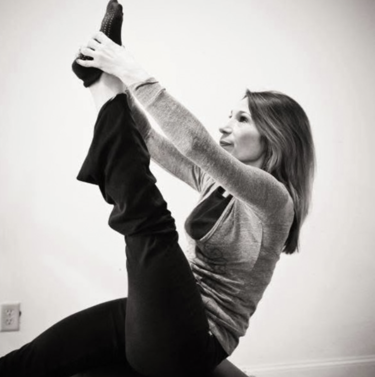 Woman in activewear performing a seated forward stretch exercise, holding her foot with both hands.