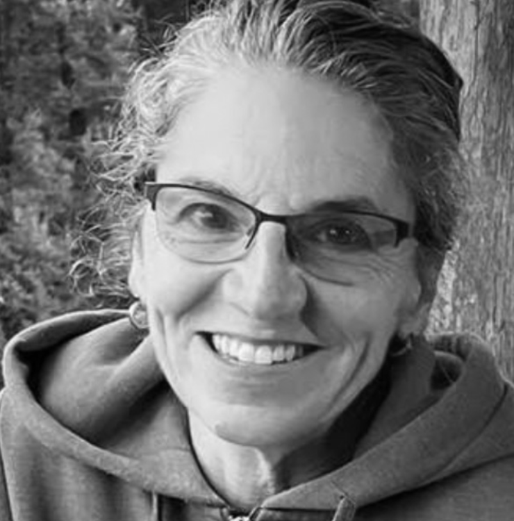 A smiling woman with short, wavy hair wearing glasses and a hoodie.