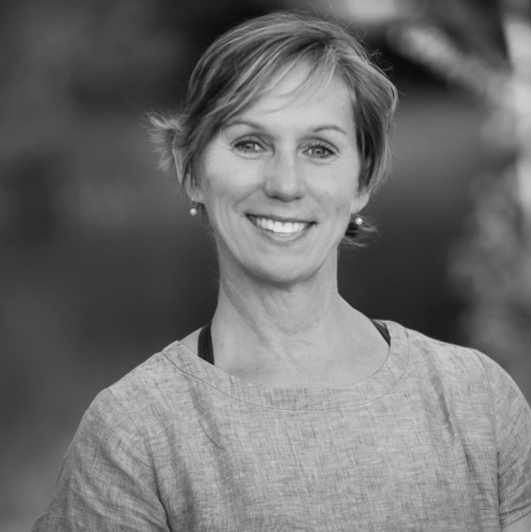 A woman with short hair smiling outdoors in black and white.