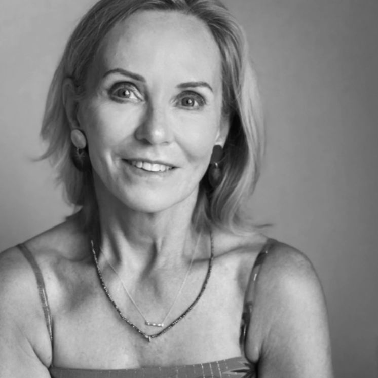 Black and white portrait of a smiling middle-aged woman with shoulder-length hair, wearing earrings, a necklace, and a sleeveless top.