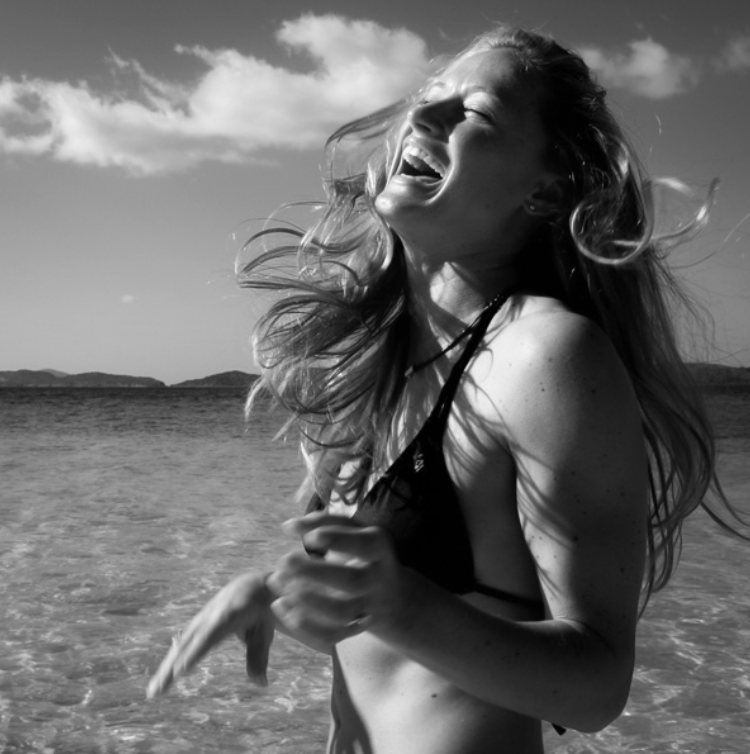 A young woman with long hair laughing joyfully on a beach in black and white.