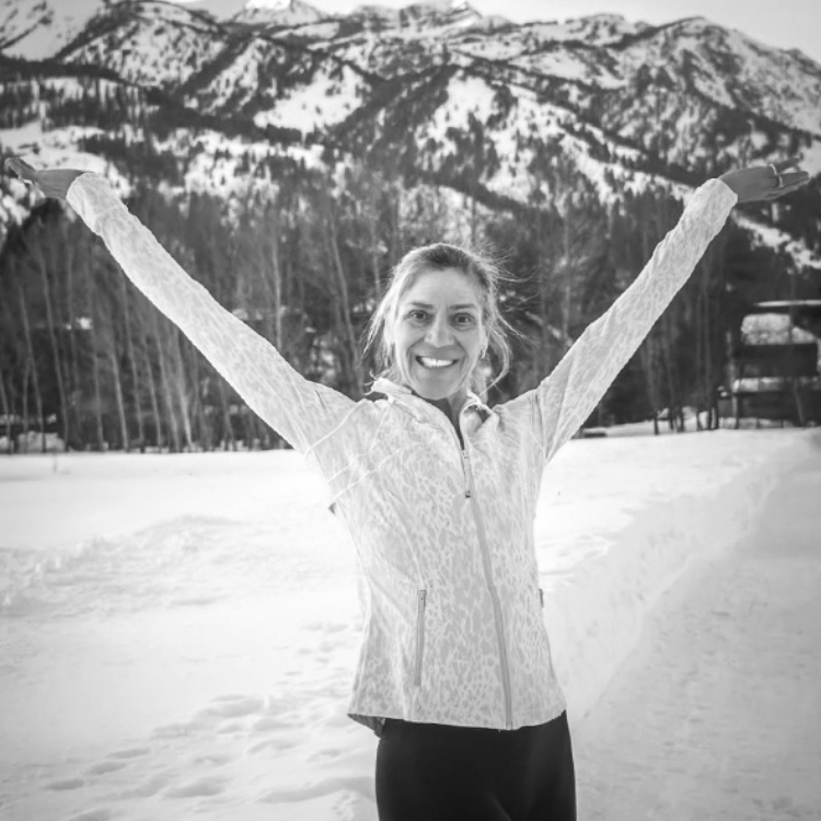 A woman with arms raised smiling in a snowy mountain landscape
