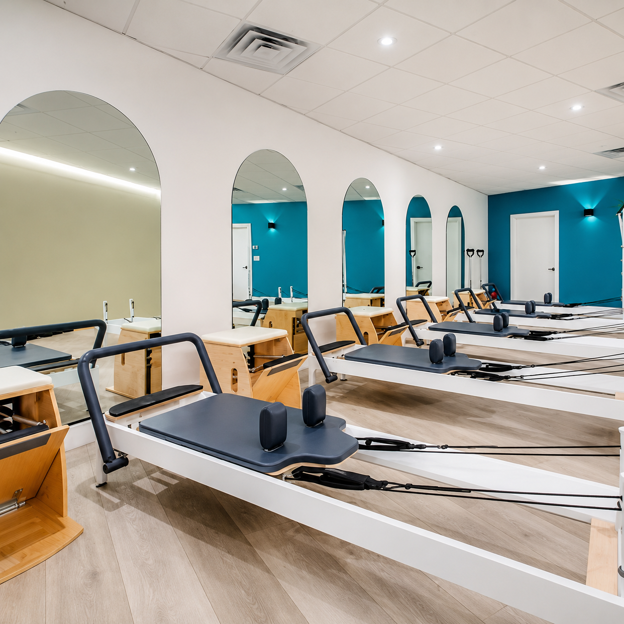 Pilates reformer exercise equipment in a fitness studio with mirrors and blue accent walls.