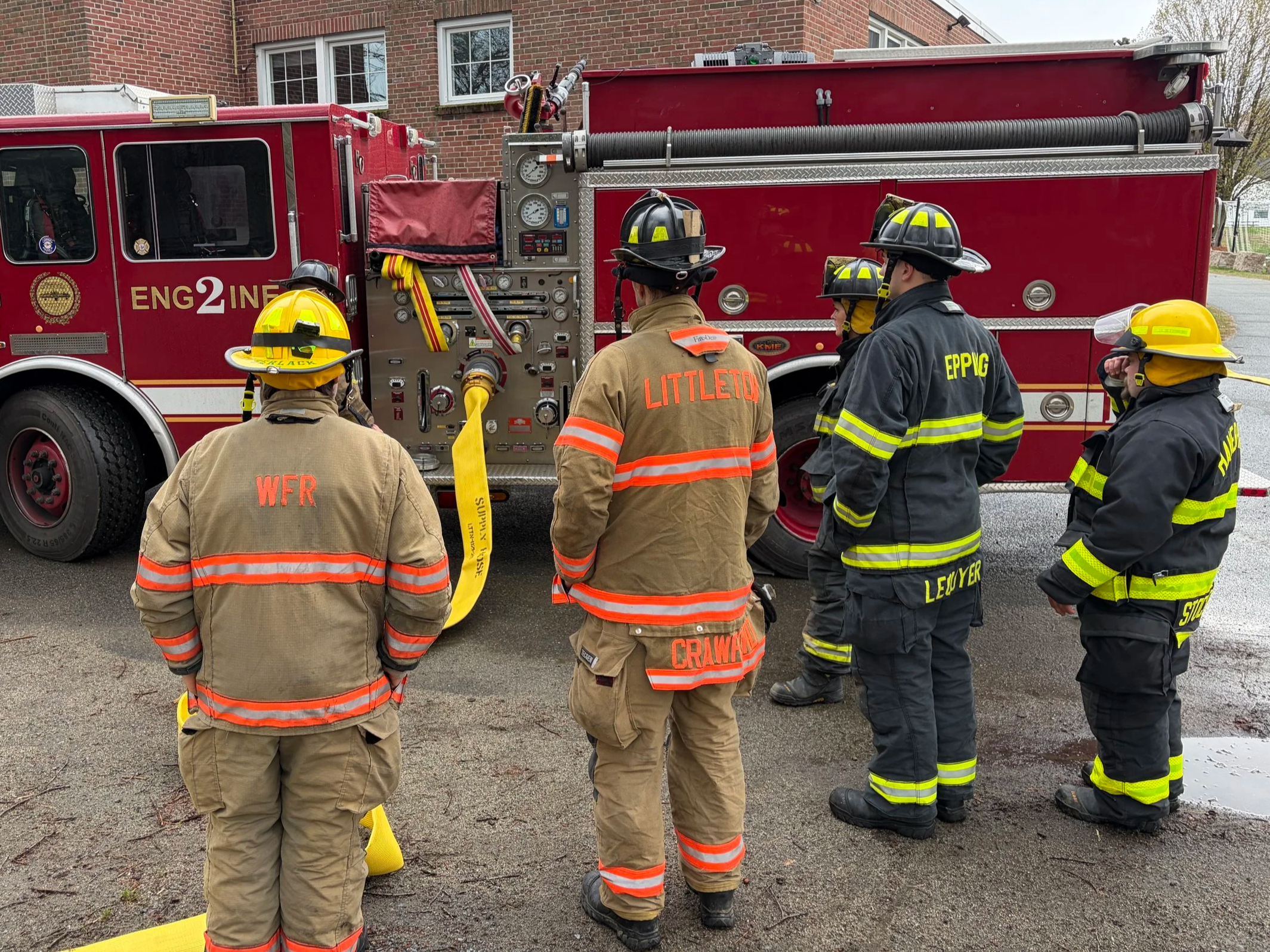 Group of firefighters in protective gear standing near a red fire truck, preparing for an emergency response.