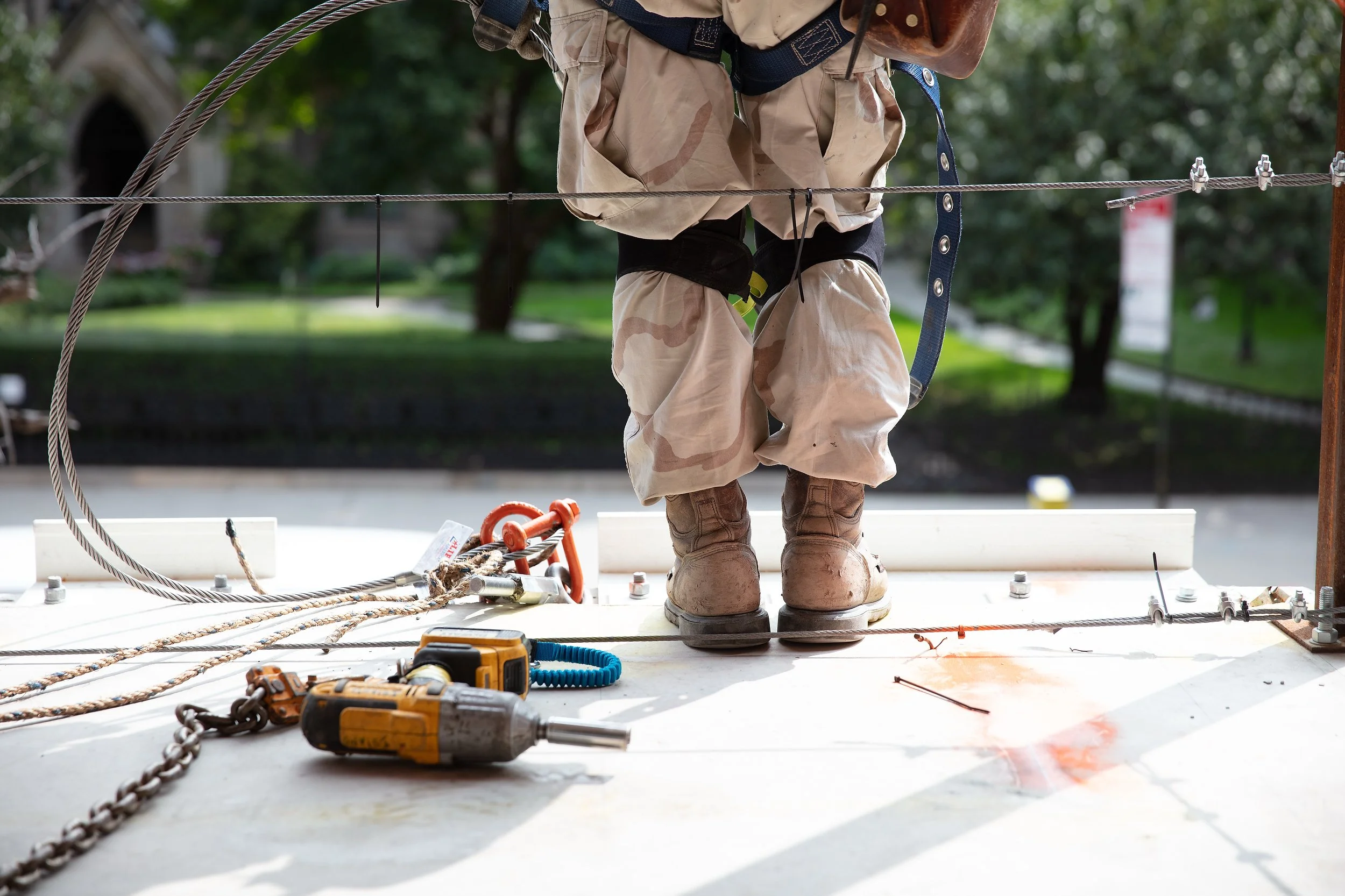 Close-up of a construction worker standing on a platform with safety harness, surrounded by tools, cables, and engineering equipment during a construction project outdoors.