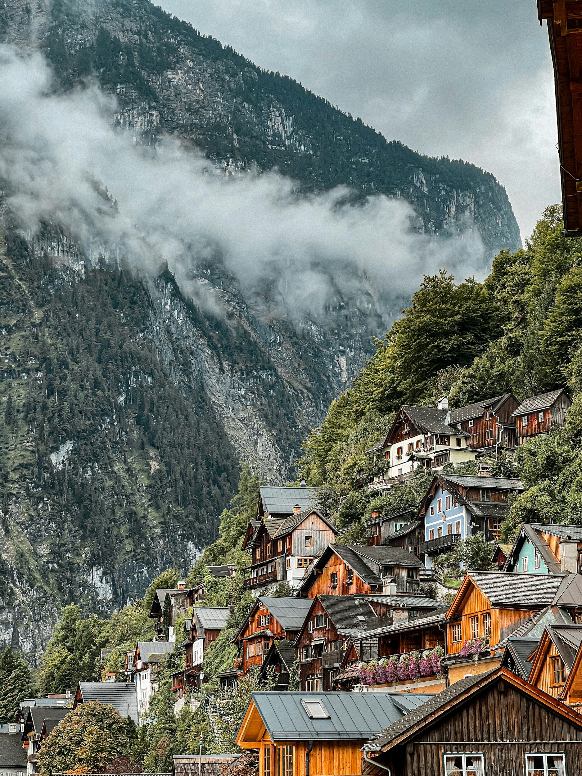 A mountainside village with colorful houses on a steep hill, surrounded by lush greenery and misty mountain slopes in the background.