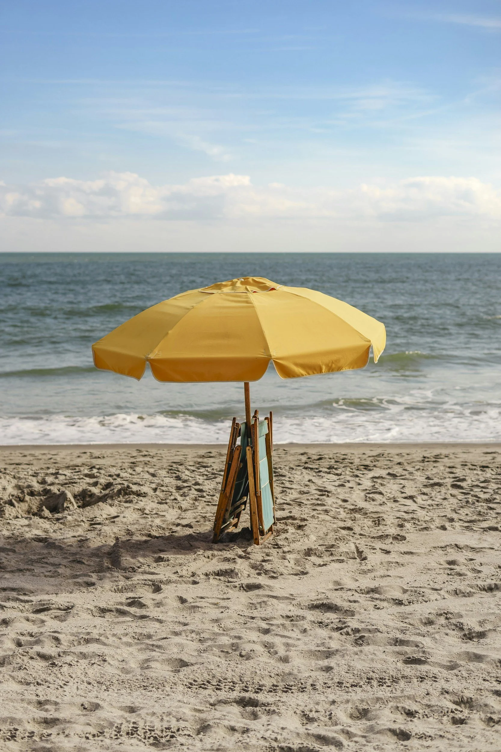 A yellow beach umbrella set up on sandy beach with the ocean and blue sky in the background.