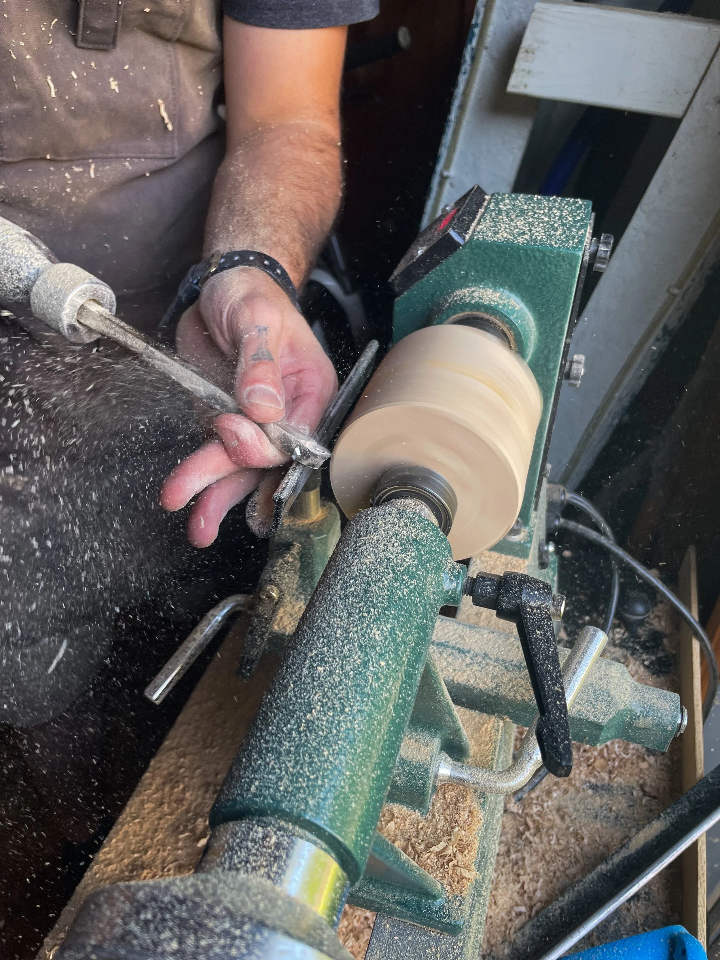 A person using a wood lathe to shape a piece of wood, creating wood shavings and sawdust in the process.