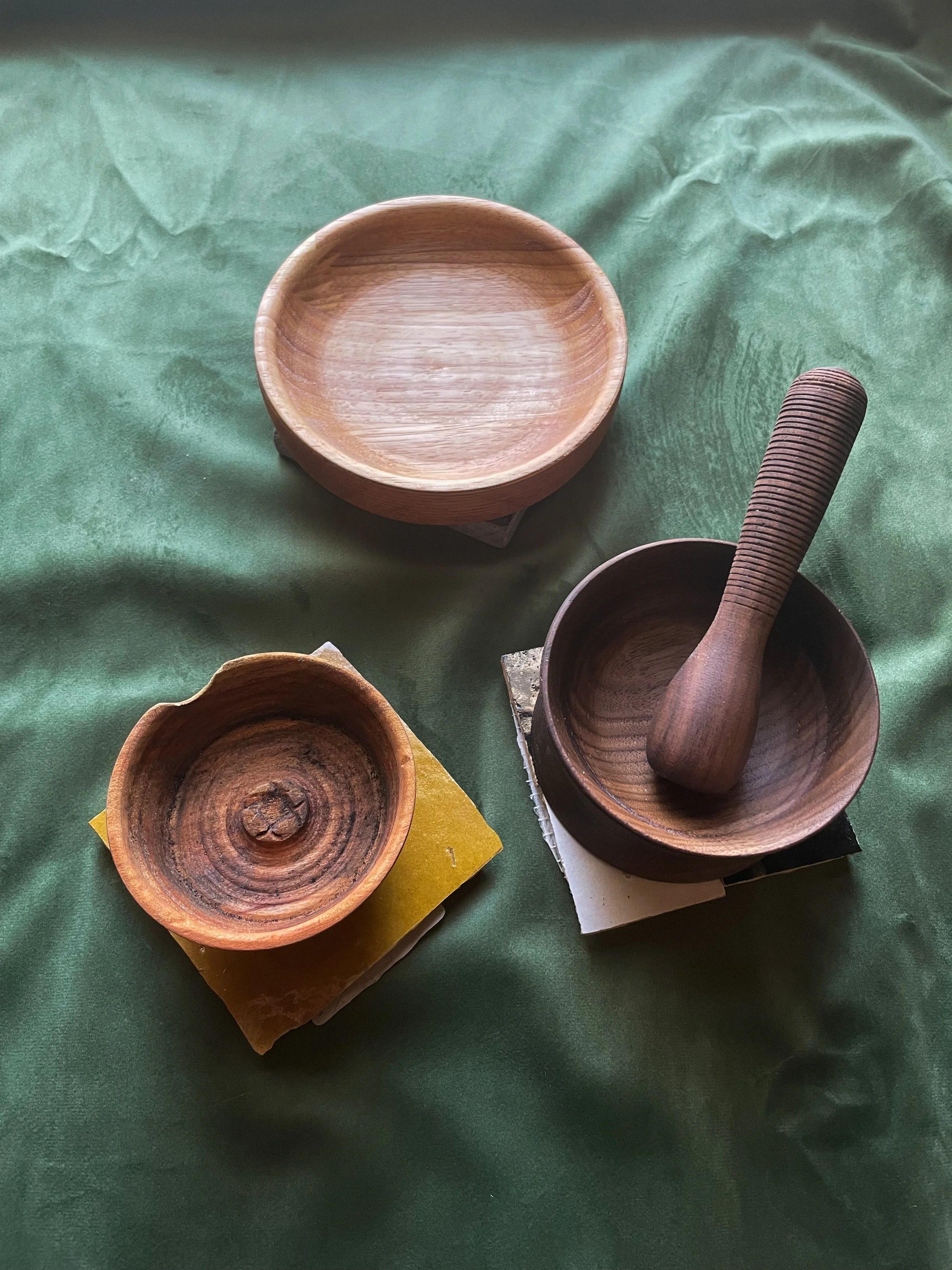 Several wooden bowls and a pestle on a green fabric background.
