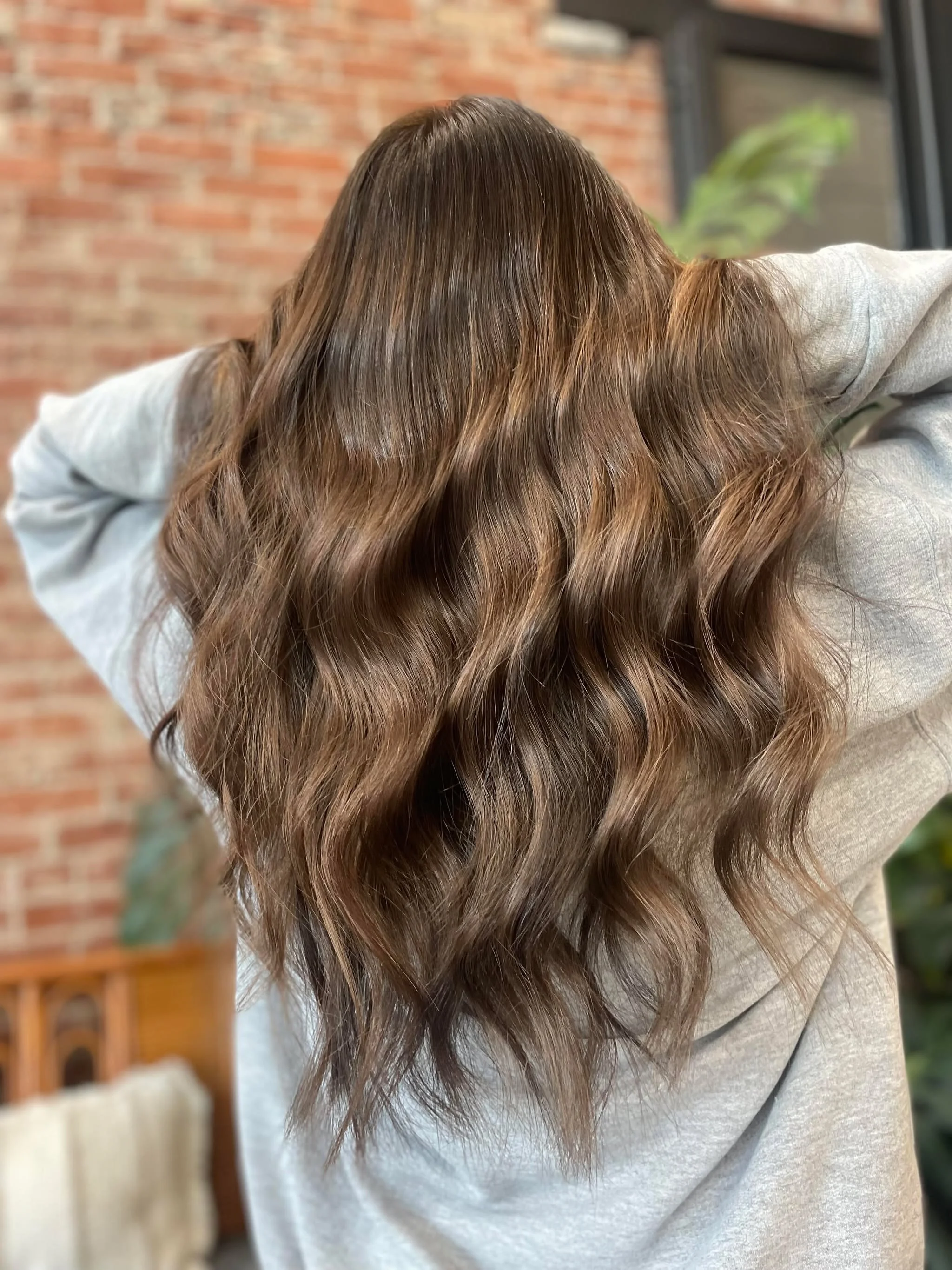 Person with long, wavy, light brown hair wearing a light-colored top, facing away.