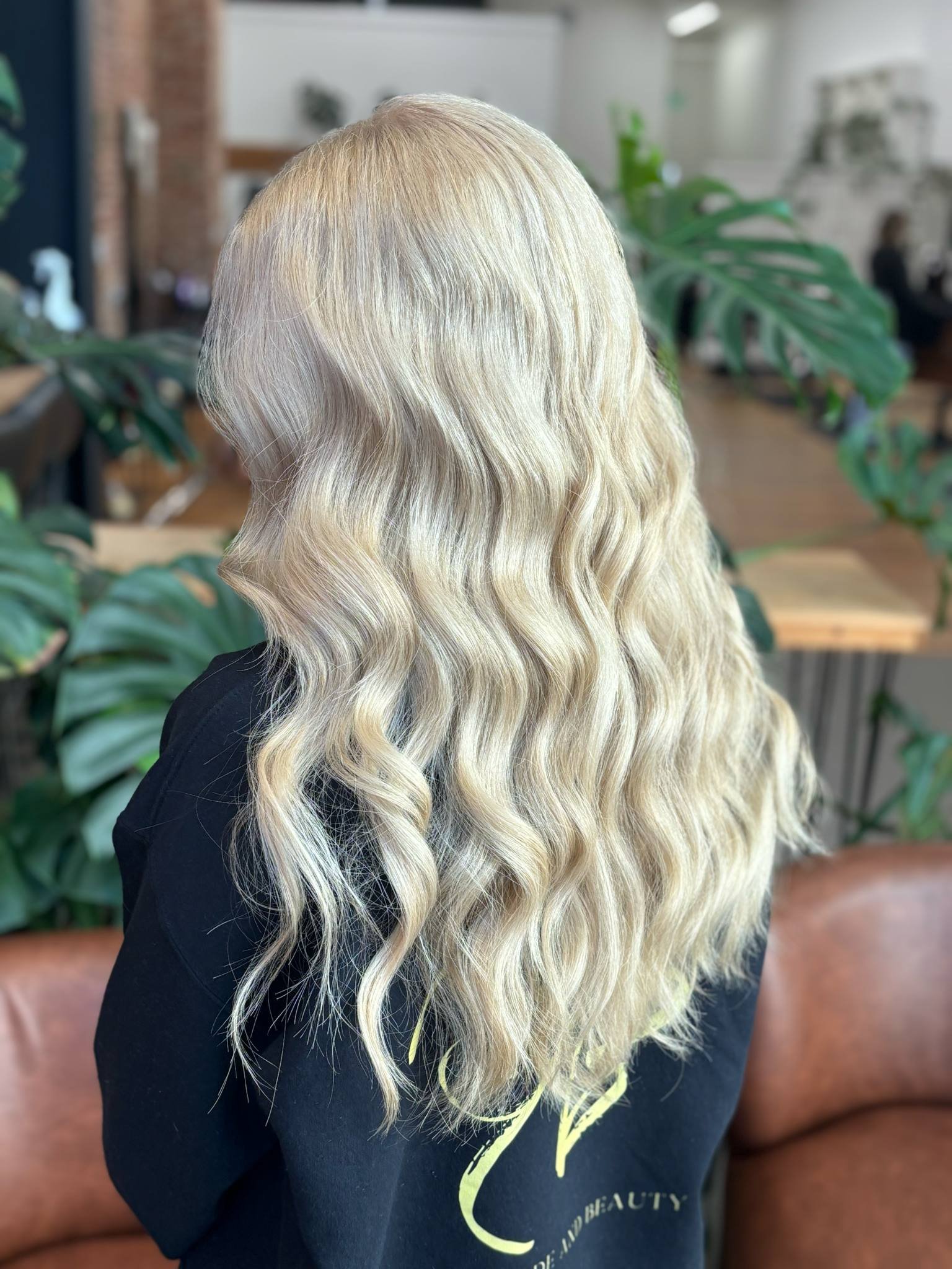 Woman with long, blonde, wavy hair sitting in a salon or hair studio.