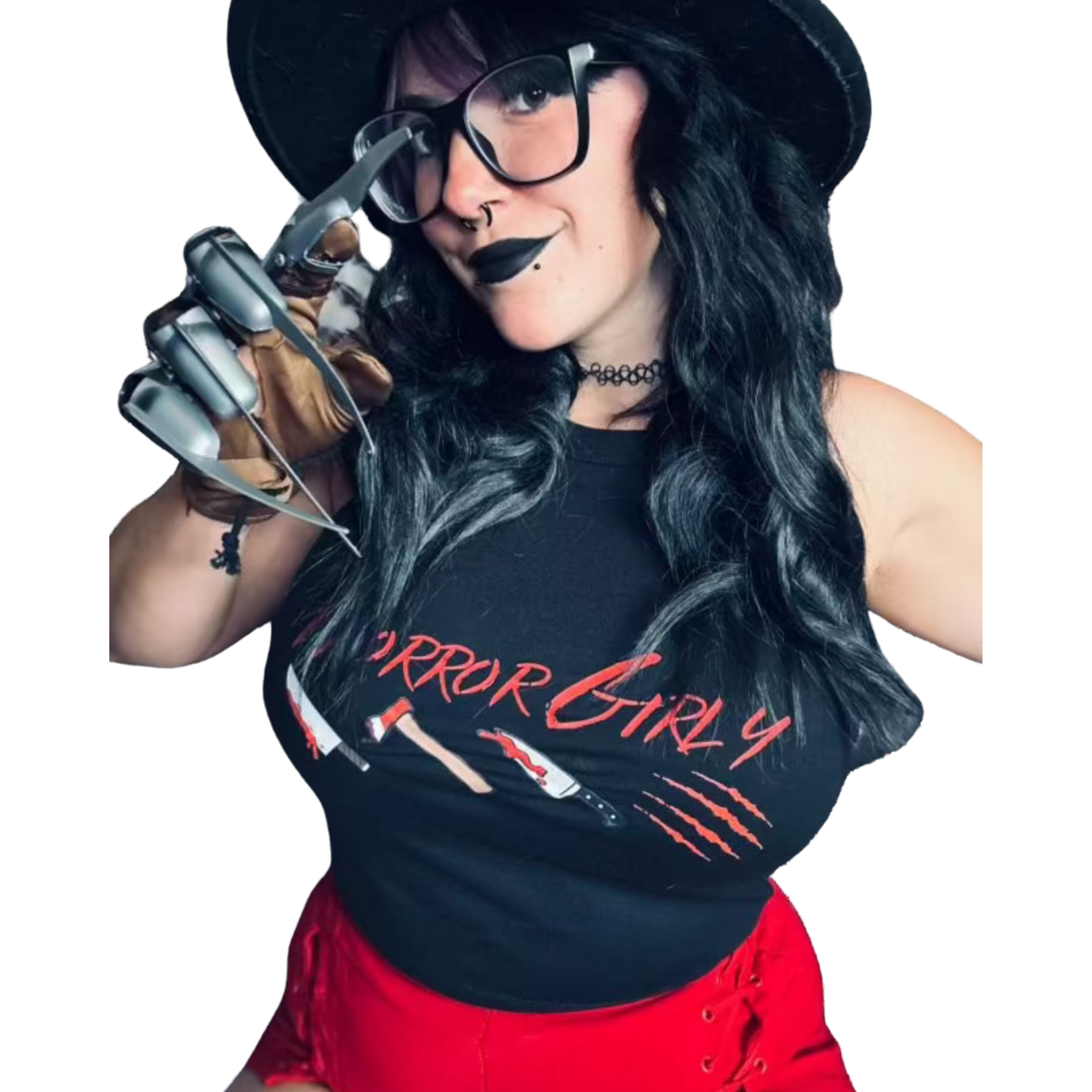 A woman with long black hair, wearing a black hat, oversized glasses, black lipstick, and a choker necklace, is holding a knife near her face. She is wearing a black top with red pants.