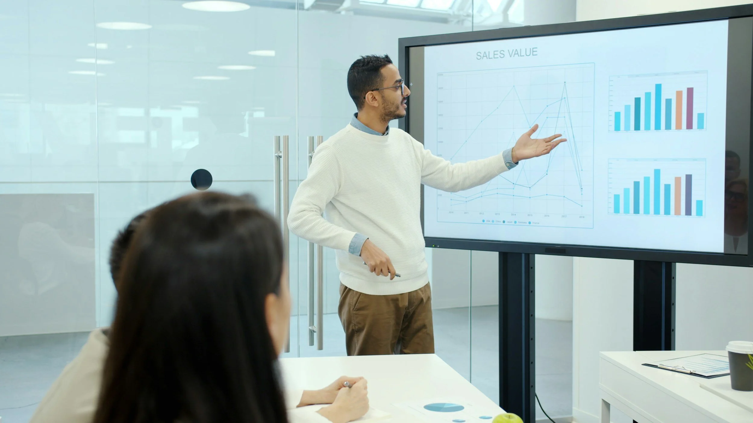 Businessman giving a presentation in a conference room with sales data displayed on a large screen.