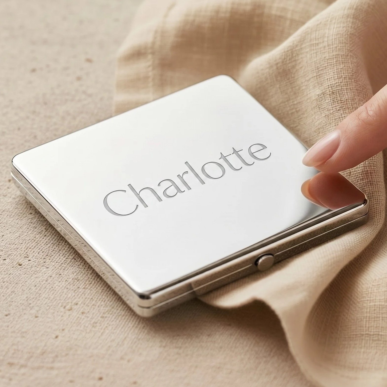 A person holding a small silver foldable mirror with the word "Charlotte" written on the reflective surface.