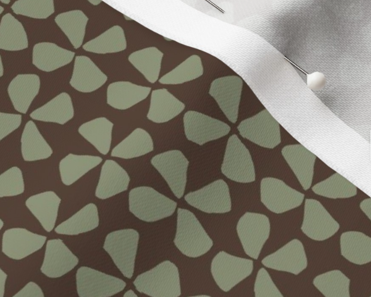 Close-up of fabric with a dark background and light green leaf-like pattern, partially covered by a white fabric with a pin.