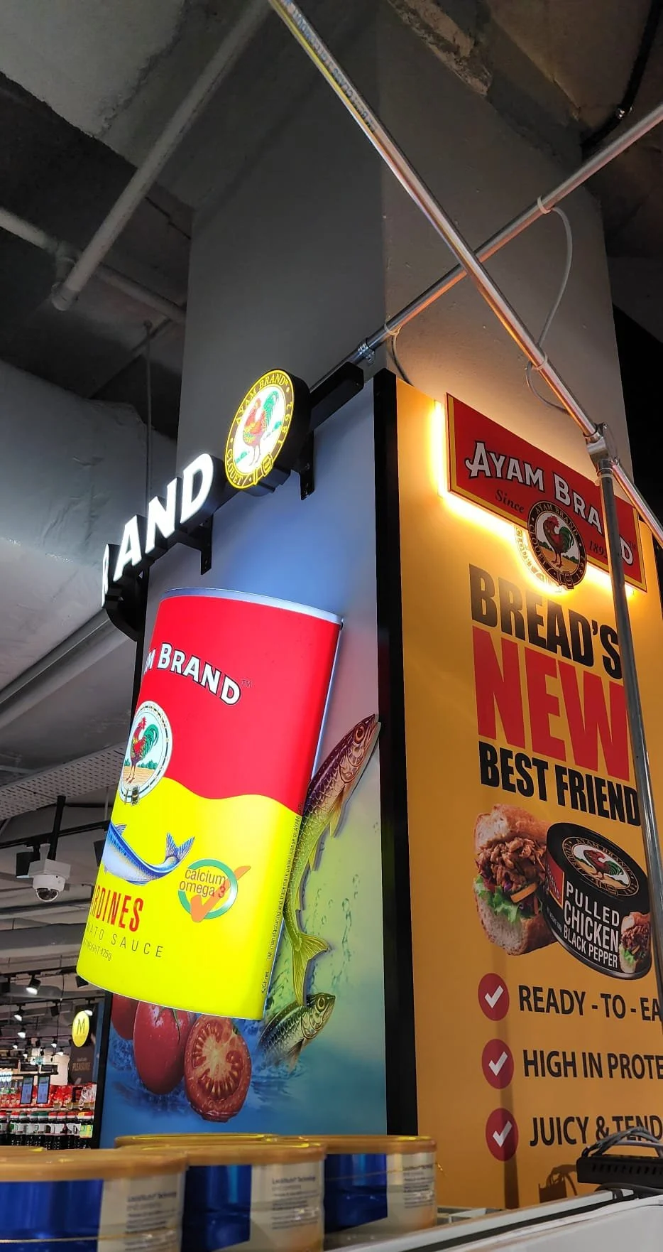 Bright yellow advertisement with red and black text for Bread's New Best Friend, pulled chicken with black pepper, featuring an image of a sandwich and a can of Sparrow Brand fish with tomatoes in the background.