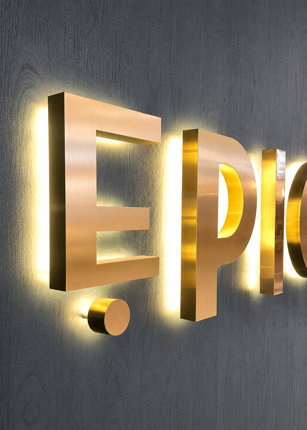 Close-up of illuminated metallic signage spelling 'EPIC' mounted on a textured dark gray wall.