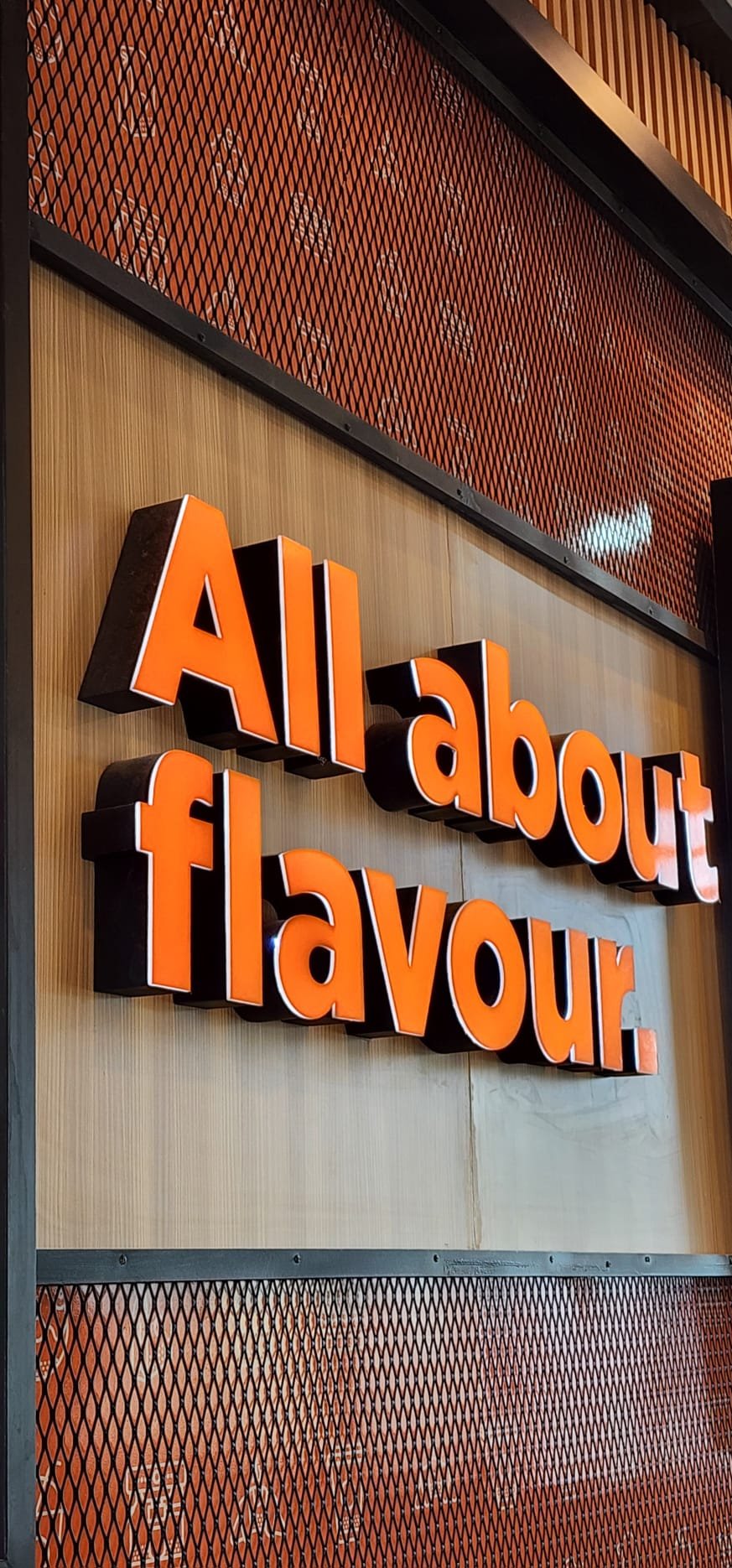 A sign with the words 'All about flavour' in orange three-dimensional letters mounted on a wooden wall.