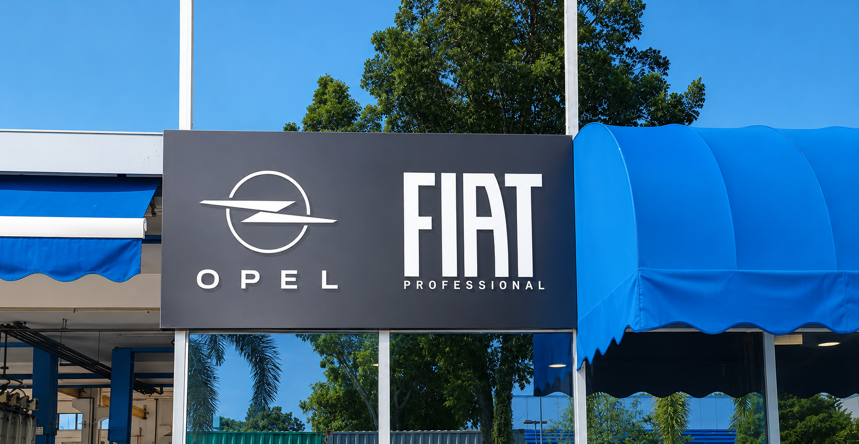 Signboard displaying Opel and Fiat Professional logos outside a building, with blue awning and green trees in the background.