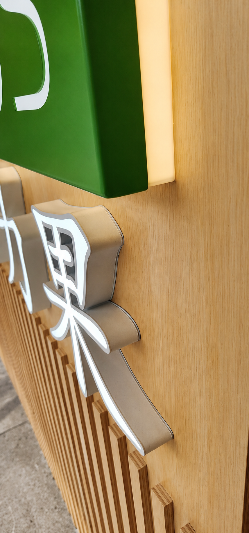 Close-up of a wall with decorative 3D letters in white and gray, a green box, a white rectangular light, and a wooden slat panel beneath.