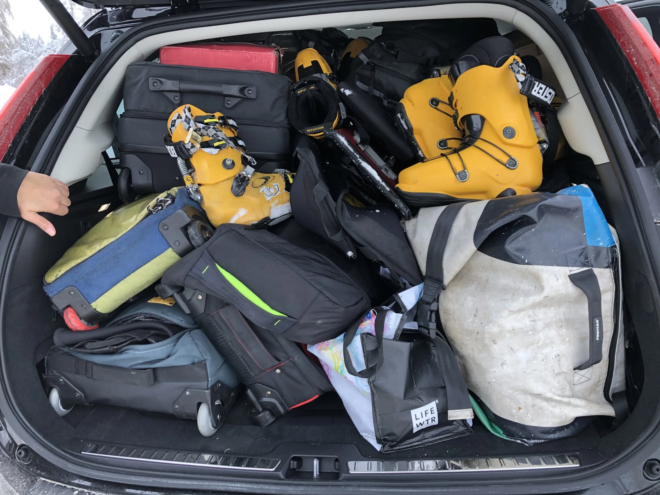 The image shows the trunk of a vehicle packed with various gear including yellow rescue boards, helmets, backpacks, a first aid kit, clothing, and other equipment, likely for outdoor or rescue activities.