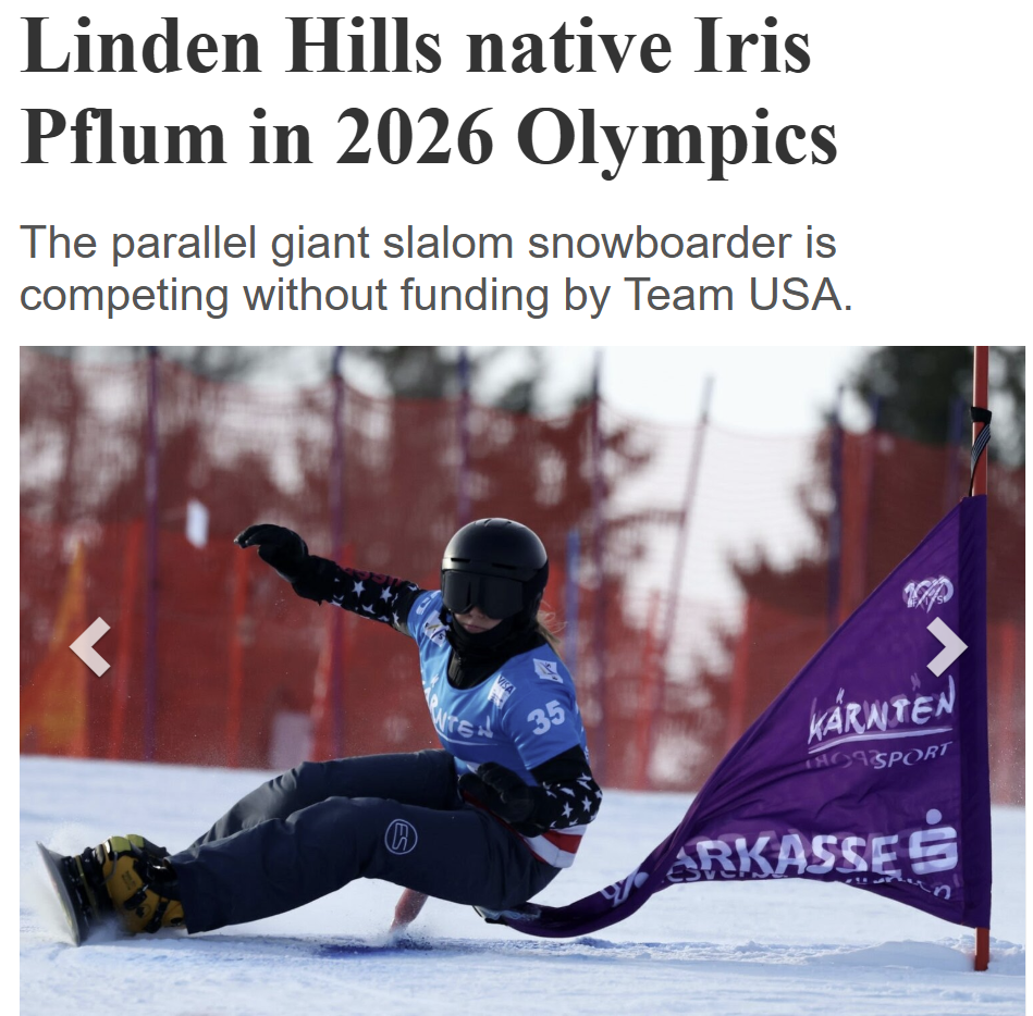 A snowboarder in a blue and black outfit with a helmet and goggles, falling on snow next to a purple race flag during a competition at the 2026 Olympics.