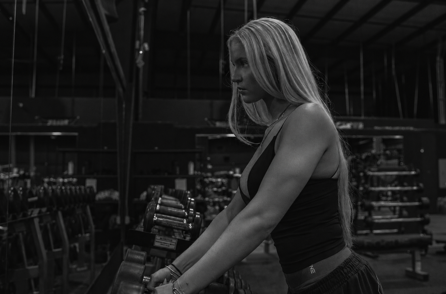 A woman with long hair, wearing athletic clothes, standing in a gym and lifting weights.