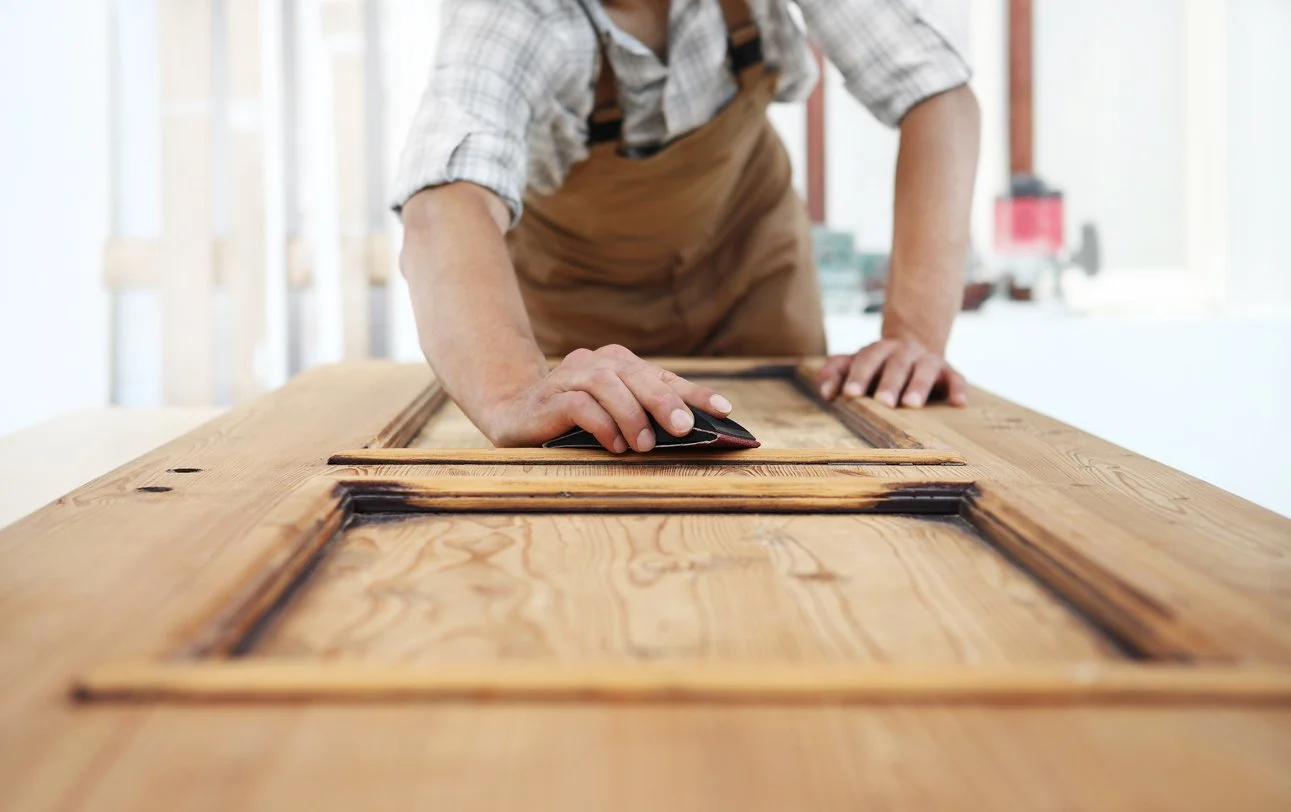 Person sanding or finishing a wooden door in a woodworking shop.