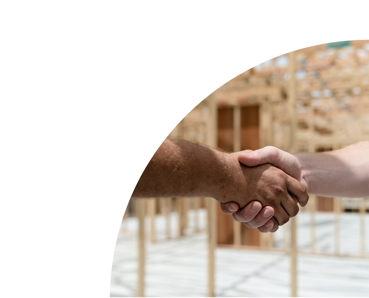 Close-up of a handshake between two people in a construction site with wood framing in the background.