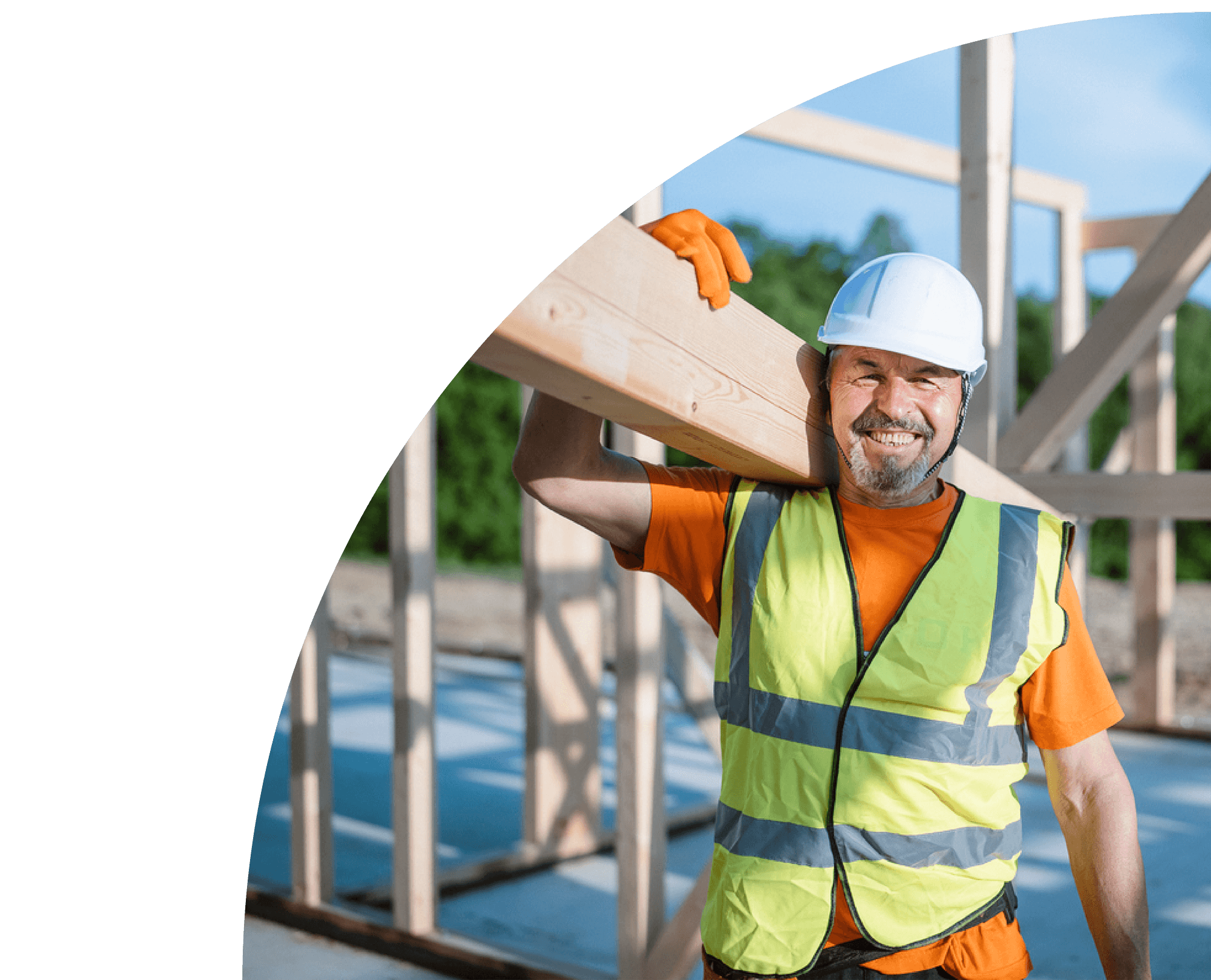 A construction worker in a white hard hat and high-visibility vest carrying a wooden plank on a building site.
