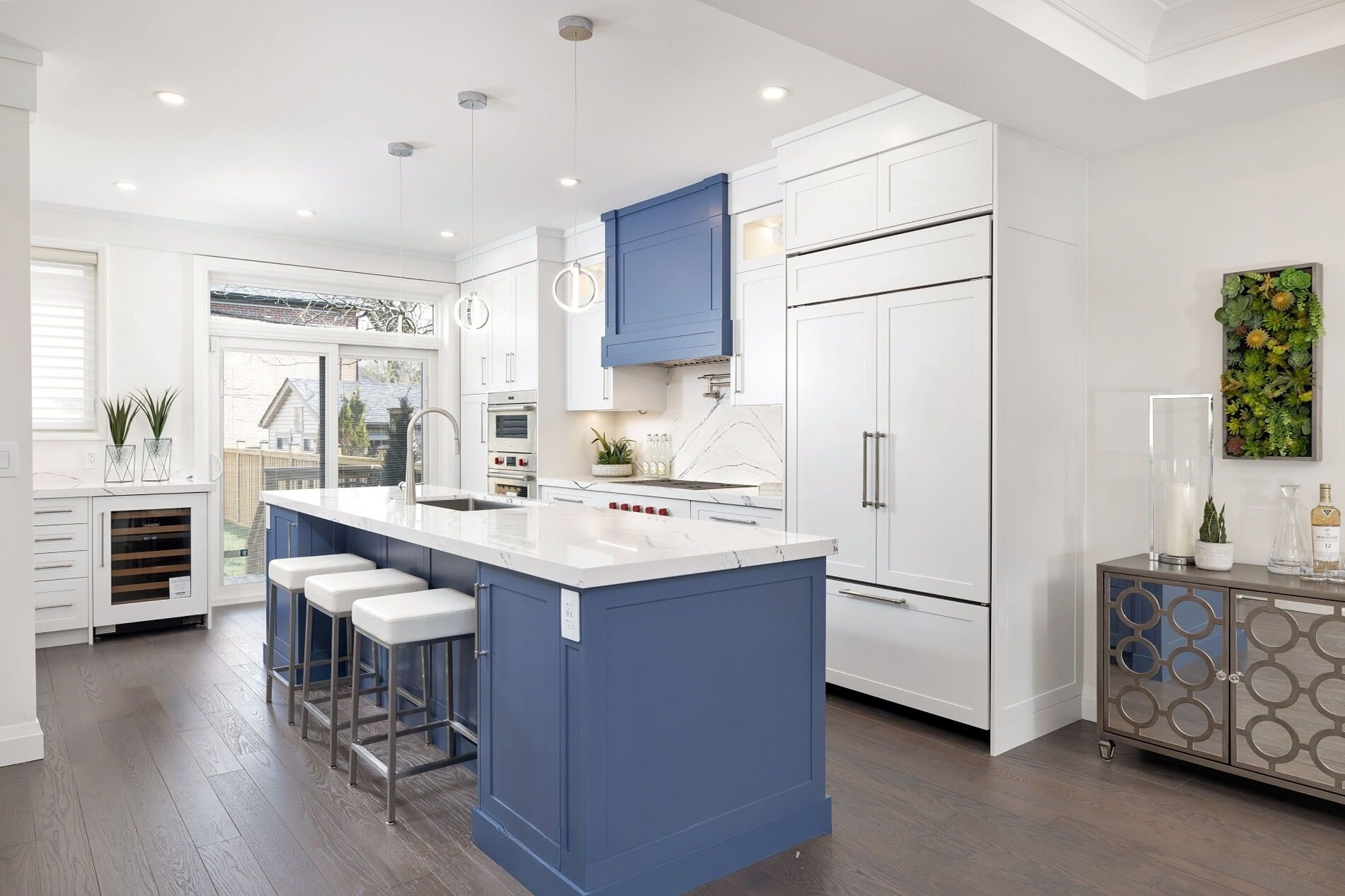 Modern kitchen with white cabinets, a blue kitchen island with seating, and a large window letting in natural light.