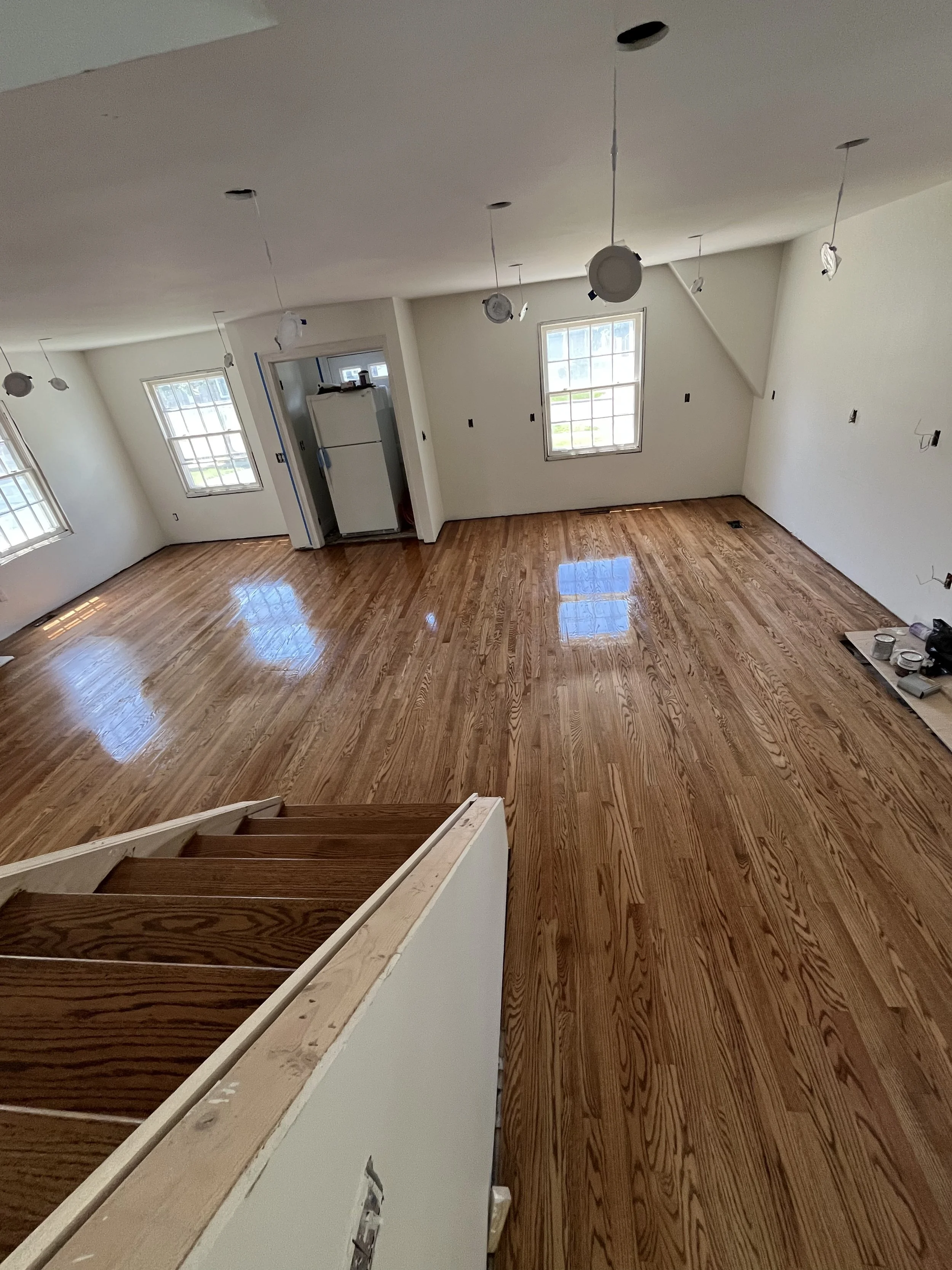 An interior room under renovation with unfinished staircase, hardwood flooring, and light fixtures hanging from the ceiling.