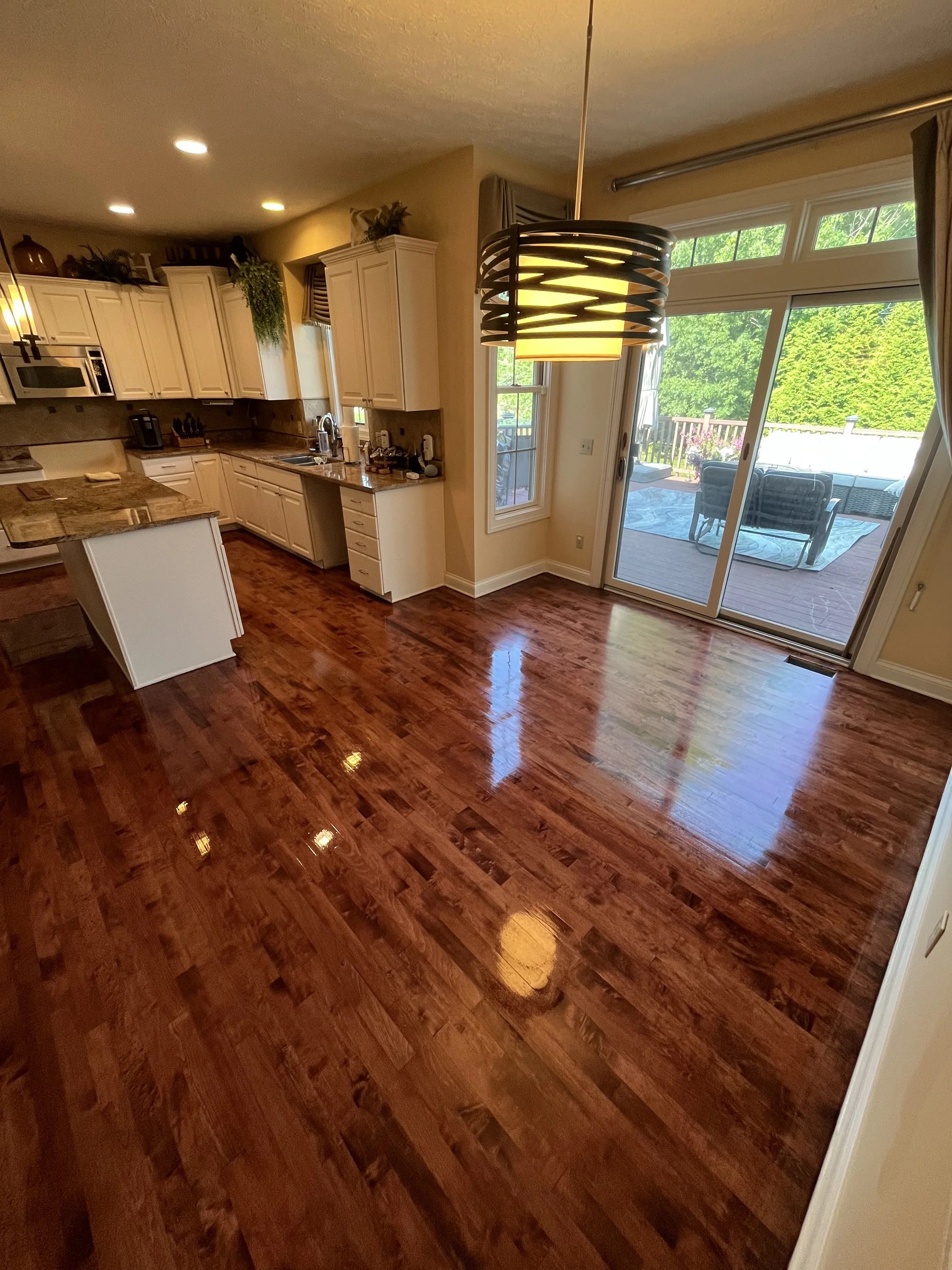 Kitchen area with hardwood floors, beige cabinets, a counter with a sink, and a sliding glass door leading to an outdoor patio with seating and greenery.
