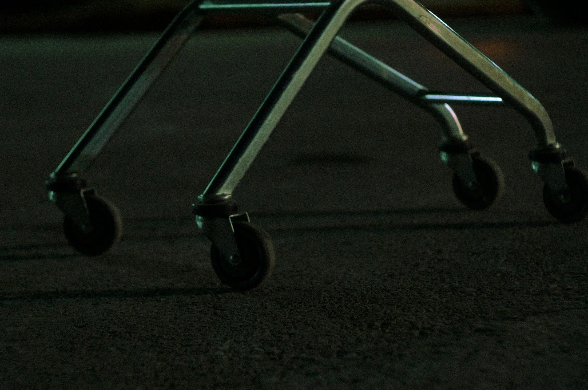A shopping cart with four wheels is on a dark surface, captured in low lighting.