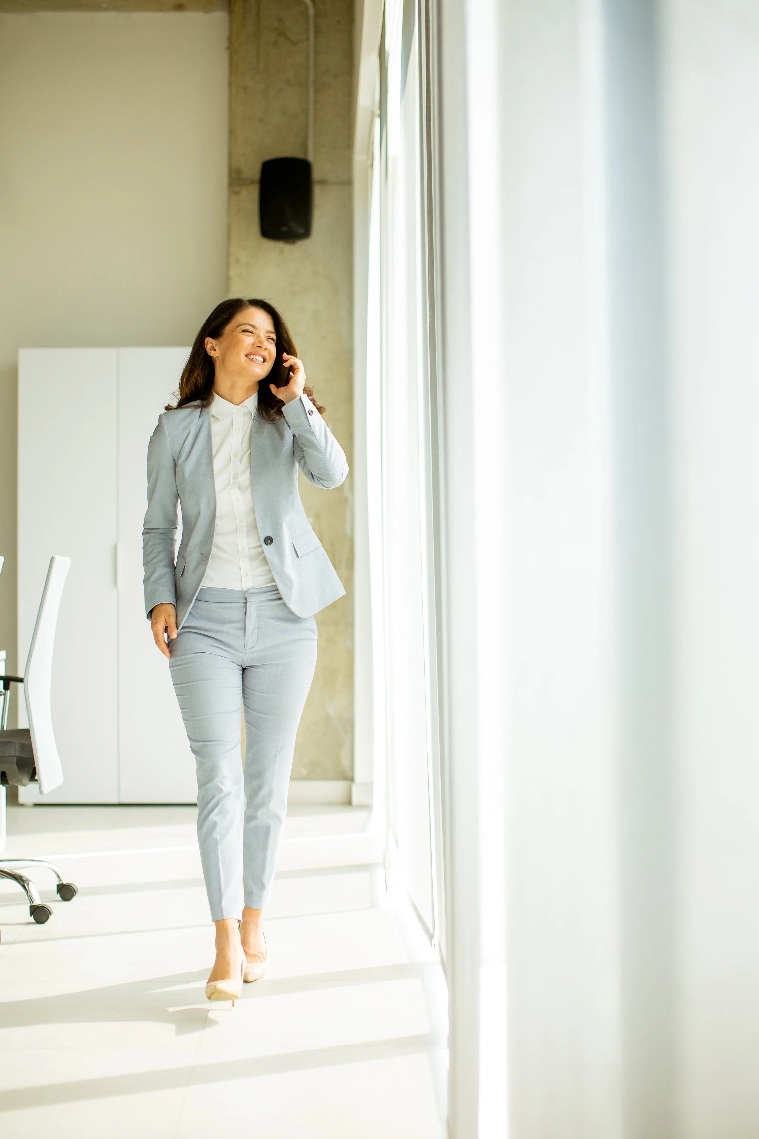 Businesswoman on phone by office window, Experience of Time Full Concierge Partnership service tier