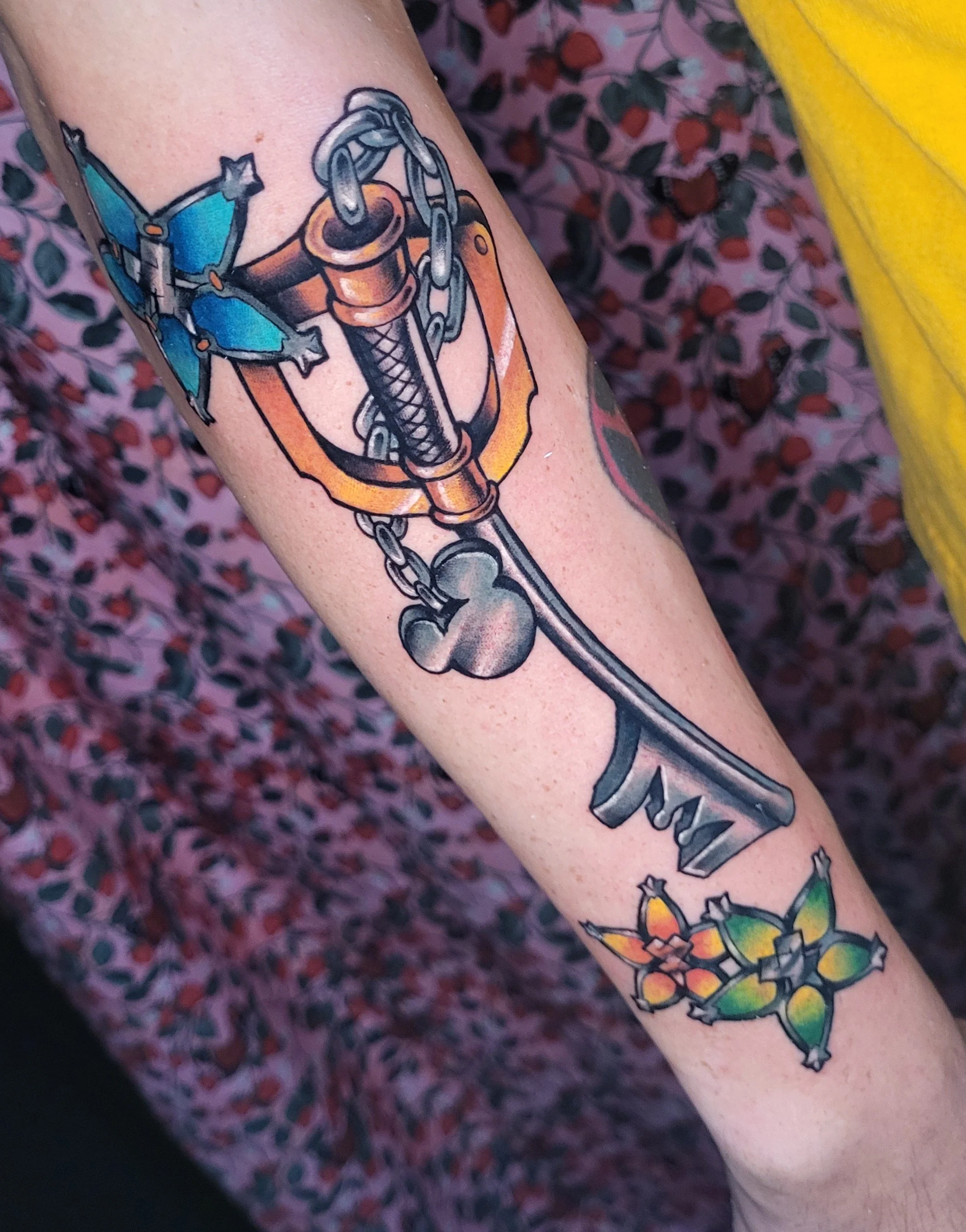 Colorful tattoo of a sword with a butterfly and plants on a person's forearm.