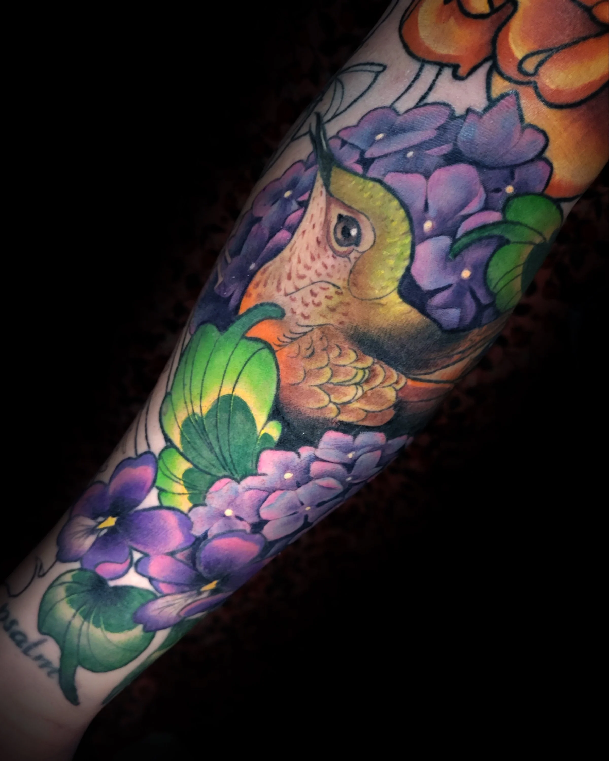 Colorful tattoo of a fish, purple flowers, and green leaves on a person's arm.