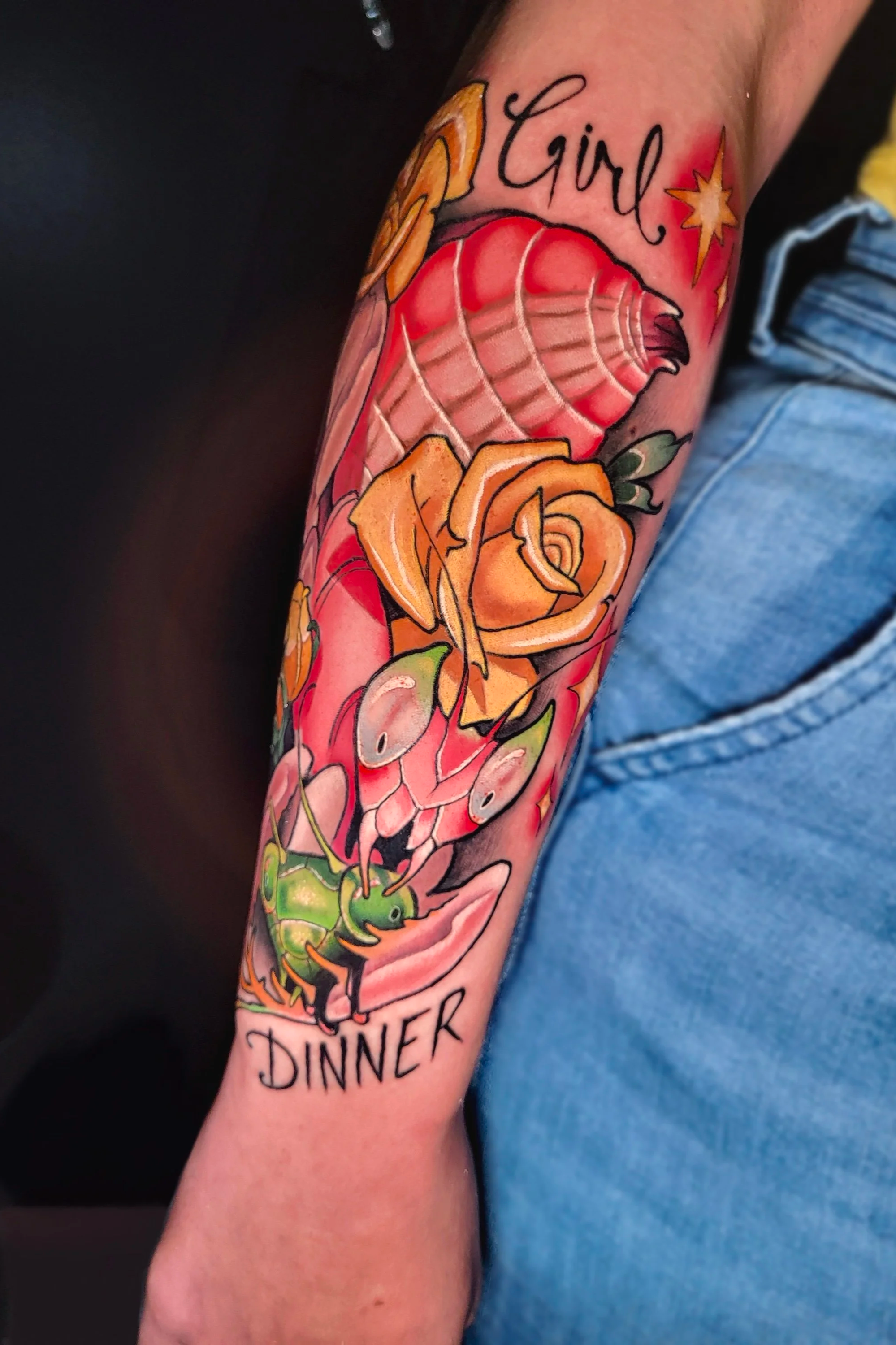 Tattoo on person's forearm featuring a large red apple, orange roses, a green ant, and the words 'Girl Dinner' written above.
