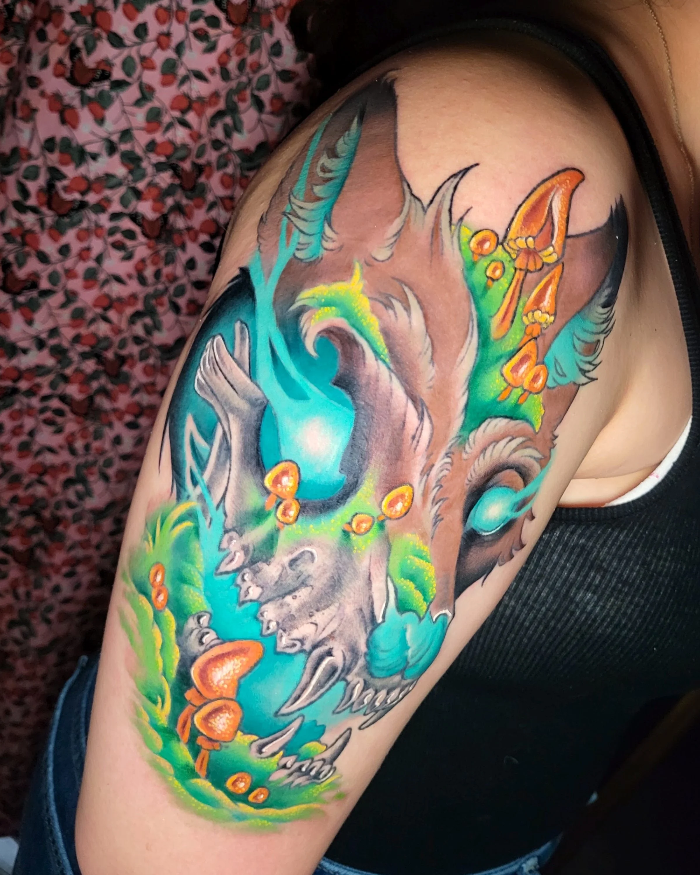 Colorful dragon tattoo on person's upper arm, featuring an orange and green dragon with a blue background and intricate details.