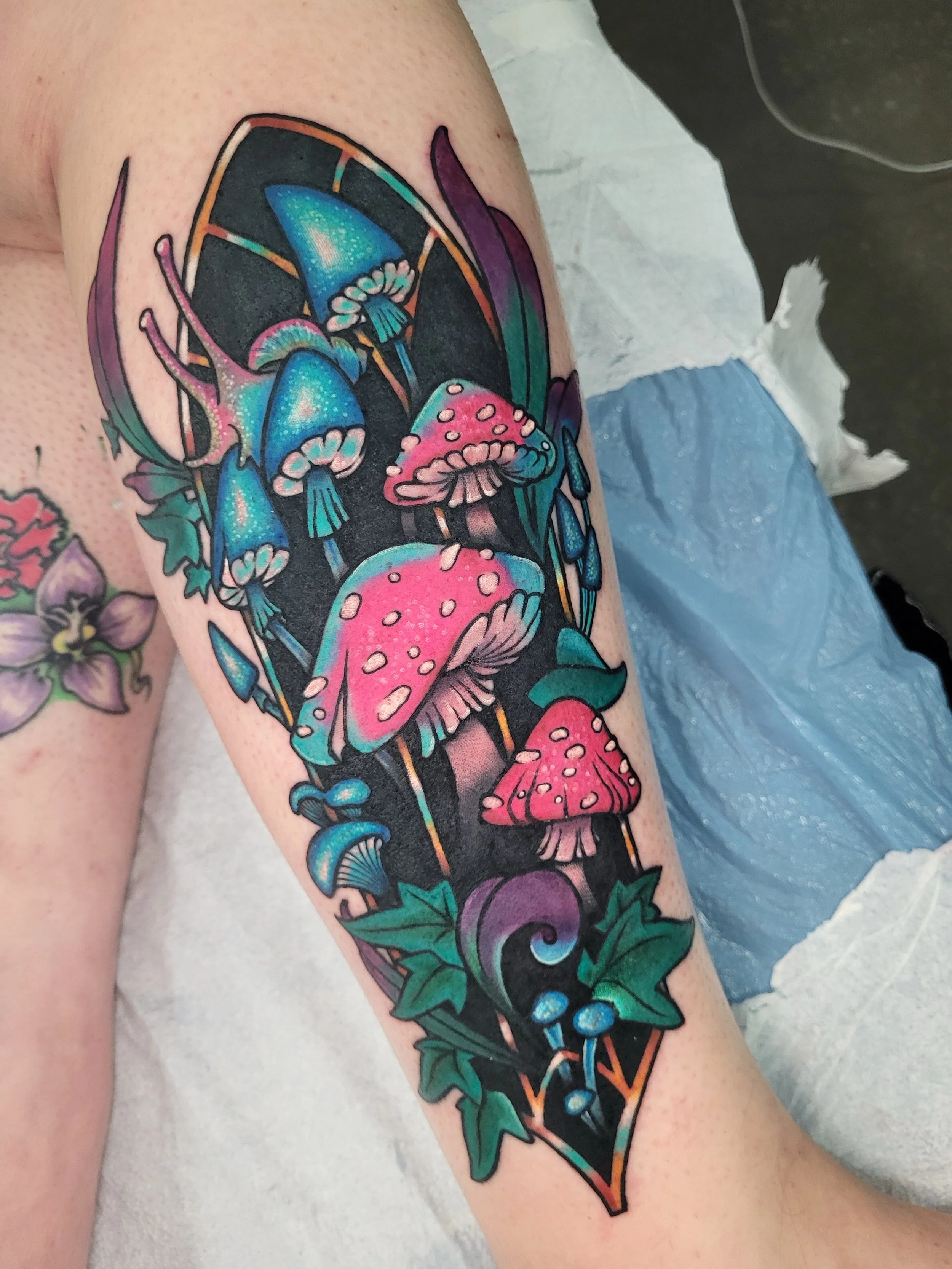 Colorful tattoo of mushrooms, leaves, and a butterfly on a person's arm.