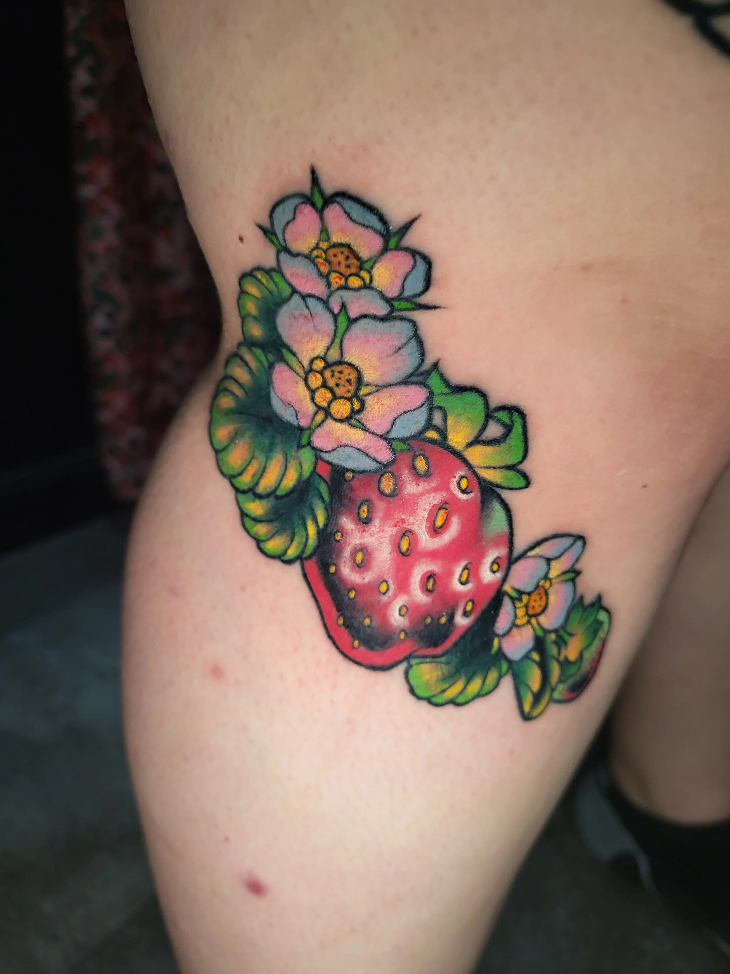 Colorful tattoo of strawberries and flowers on skin.