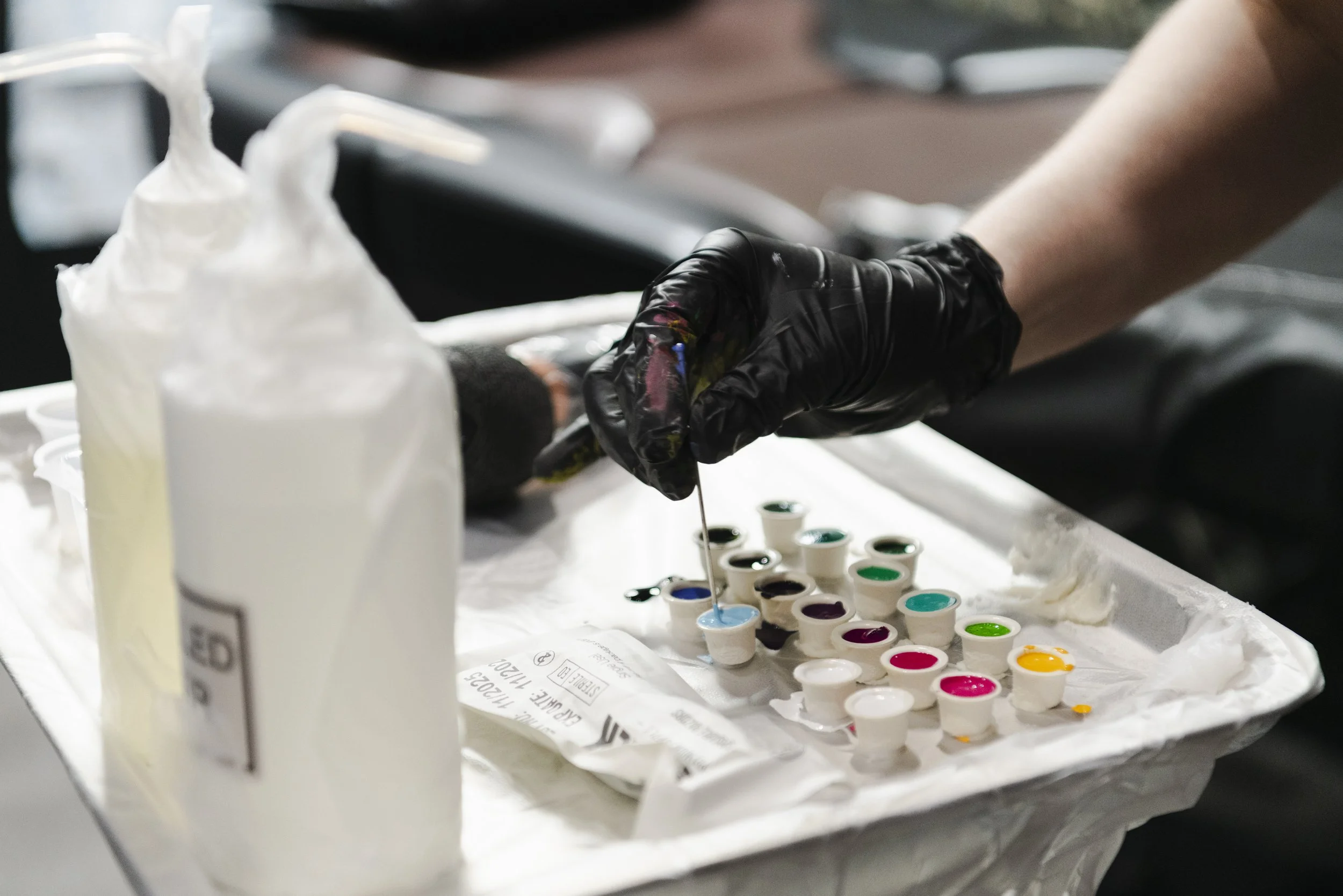 Person wearing black gloves creating colorful paint designs with watercolor paints on a table covered with a white sheet.