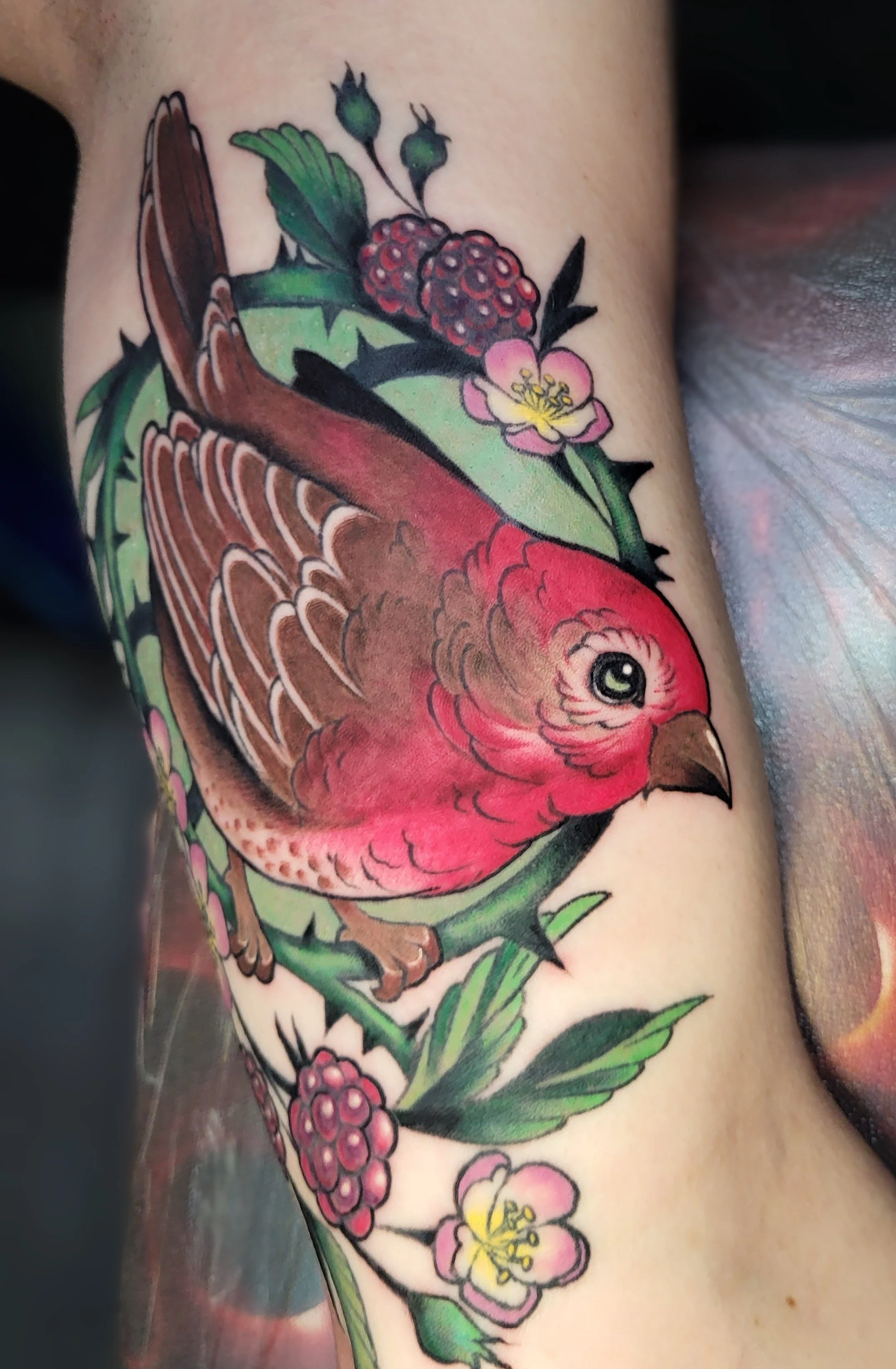 Colorful tattoo of a bird surrounded by pink and yellow flowers and green leaves.