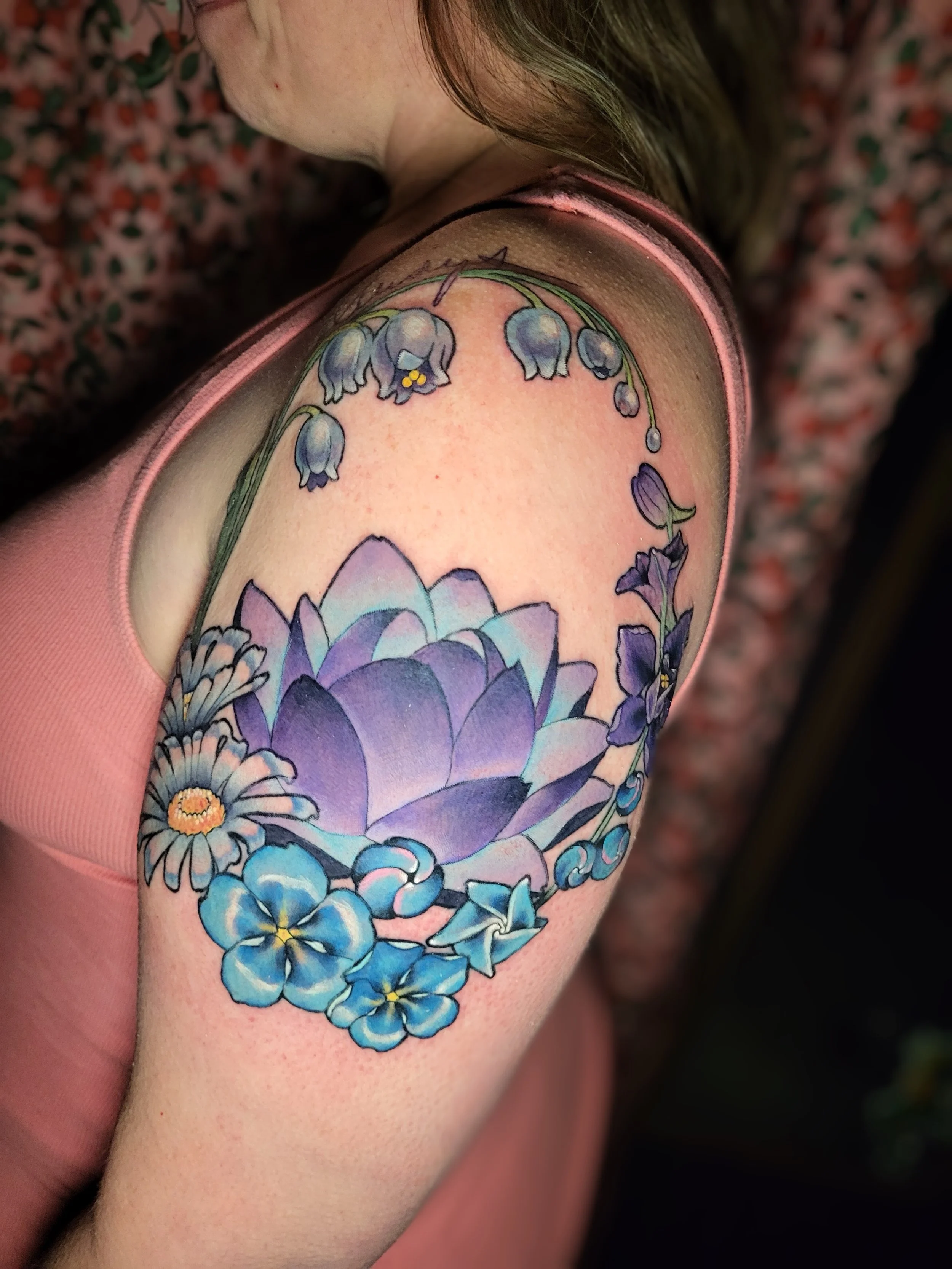 Colorful tattoo of flowers on person's upper arm with pink sleeveless shirt.