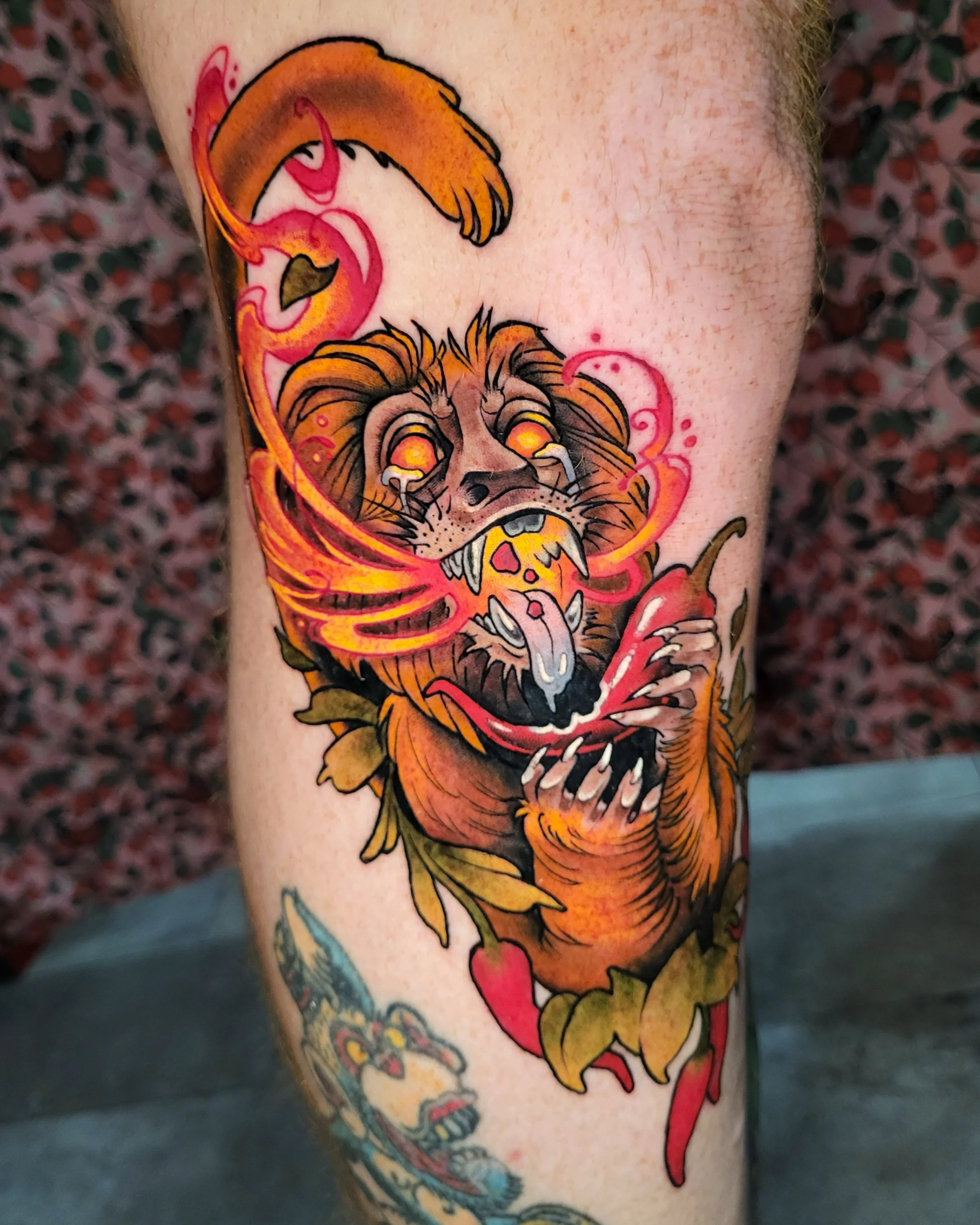 Colorful tattoo of a roaring lion with fiery orange mane and glowing eyes on a person's arm.
