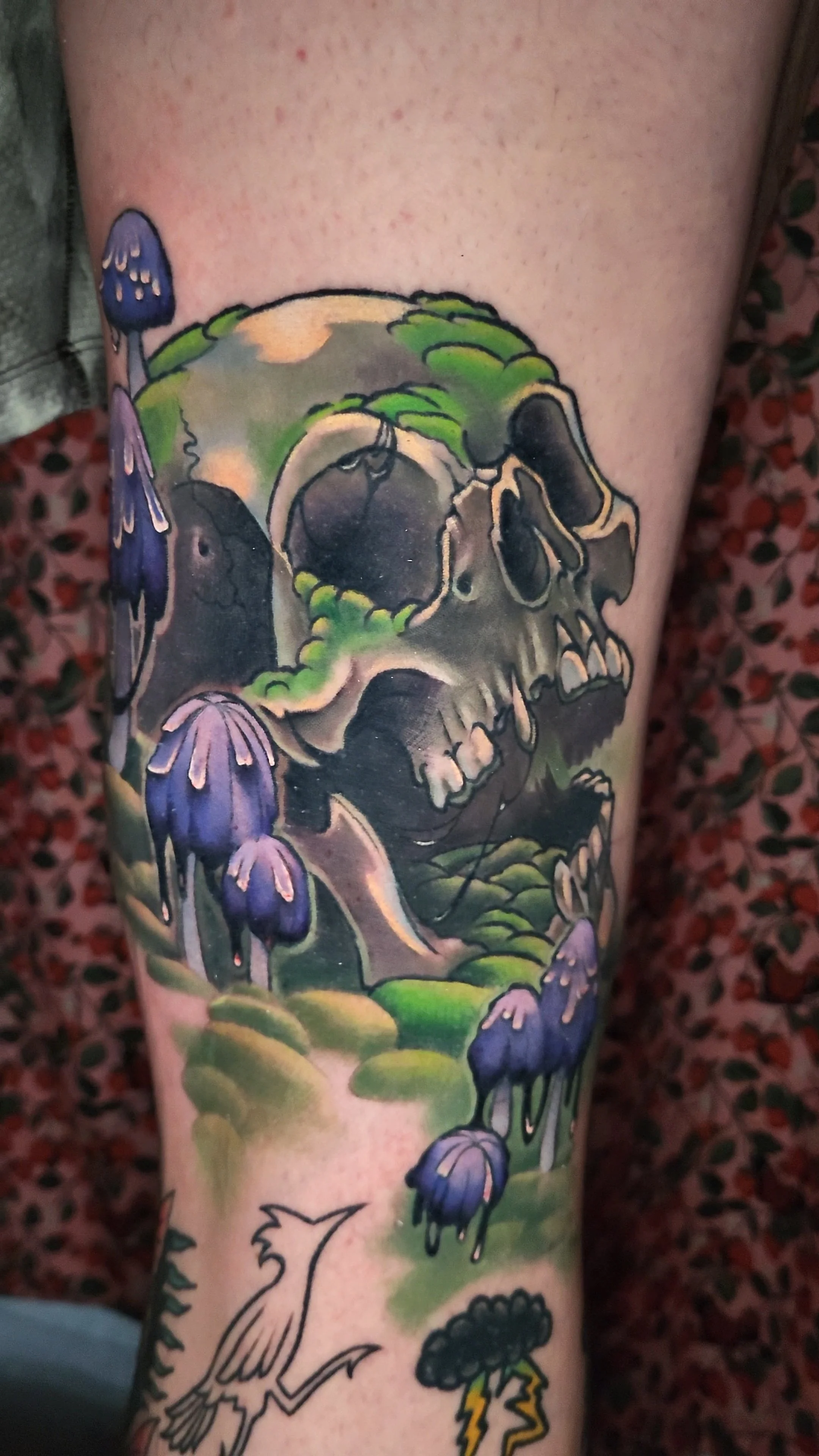 Tattoo of a skull surrounded by flowers and greenery on a person's arm.