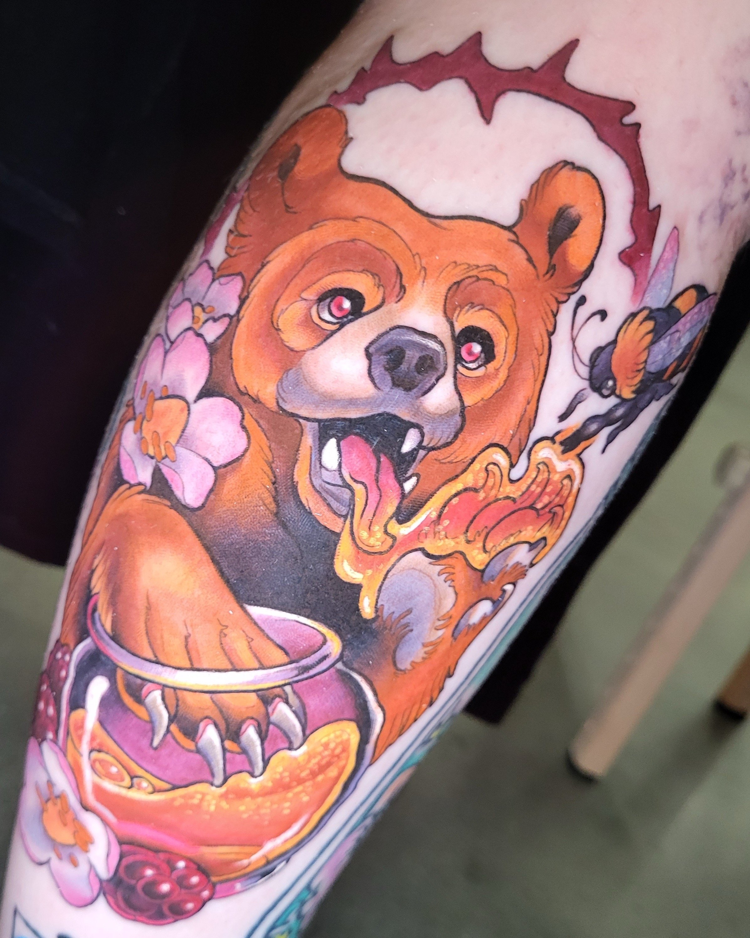 Tattoo of a fierce, animated bear with glowing eyes, surrounded by pink cherry blossoms and red berries.